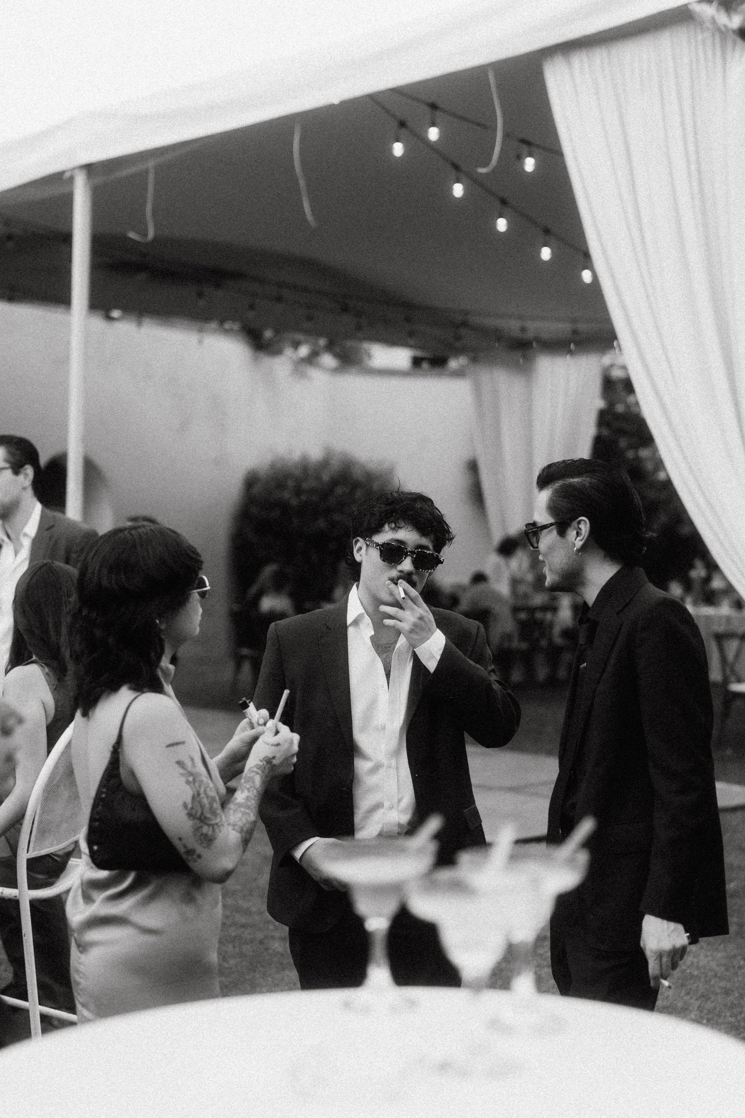 Wedding guests dancing and socializing at an elegant reception under white drapes and string lights.