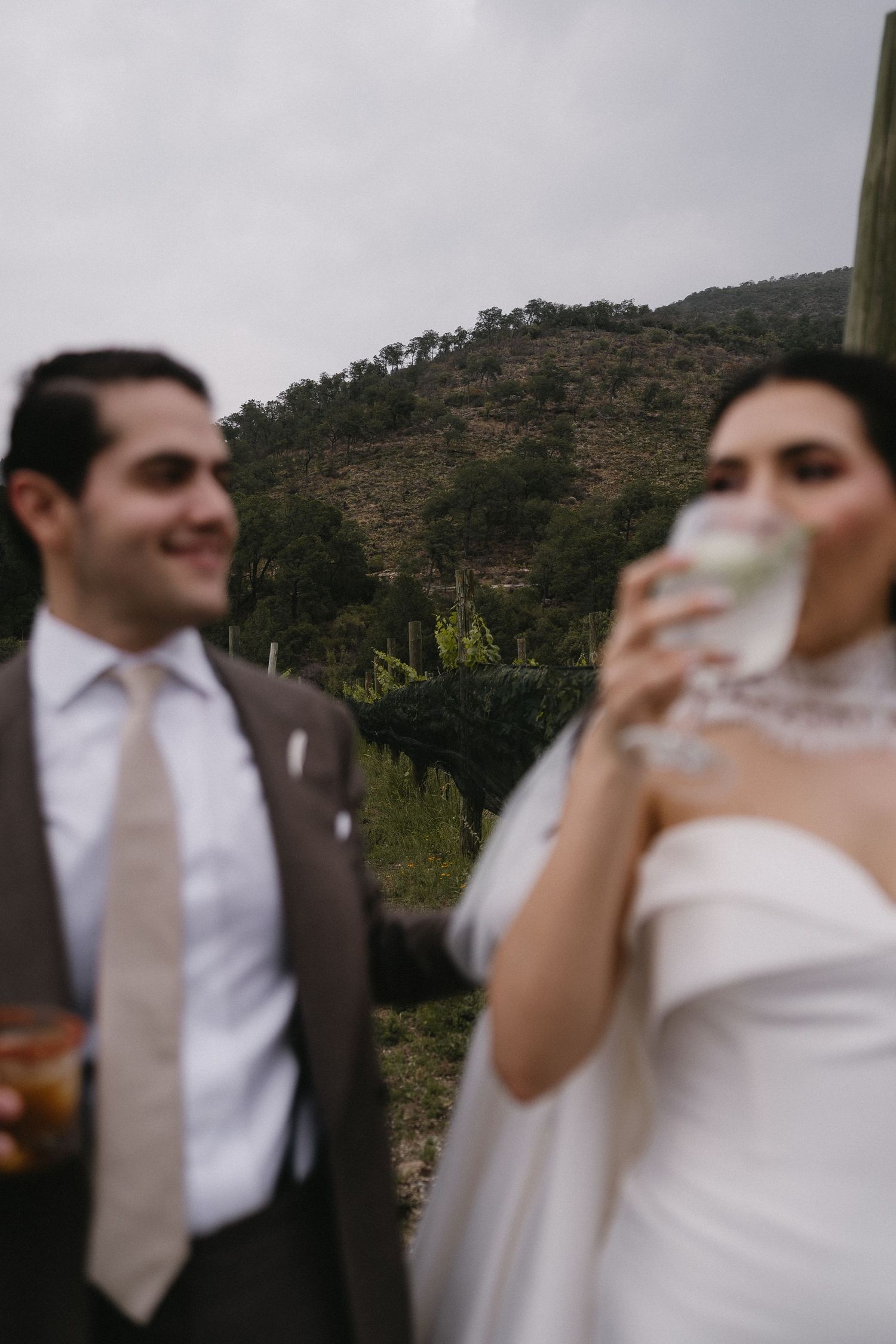 Newlyweds sharing a celebratory toast outdoors with mountain backdrop.
