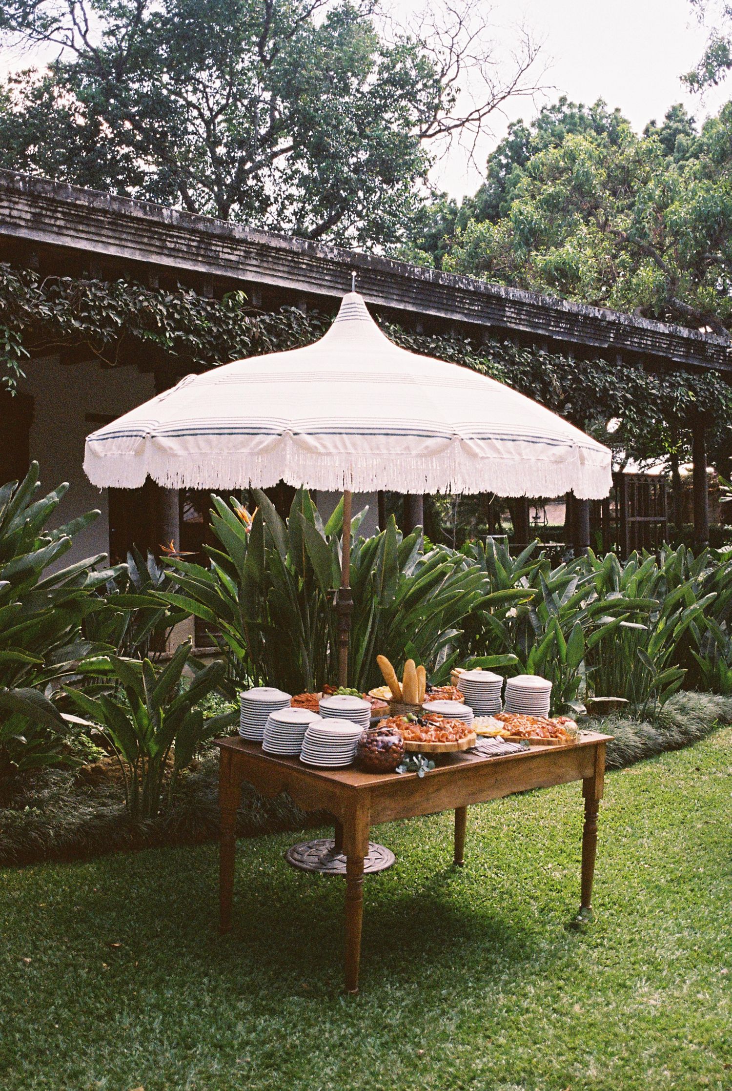 White umbrellas shade elegant buffet tables set up on a manicured lawn.