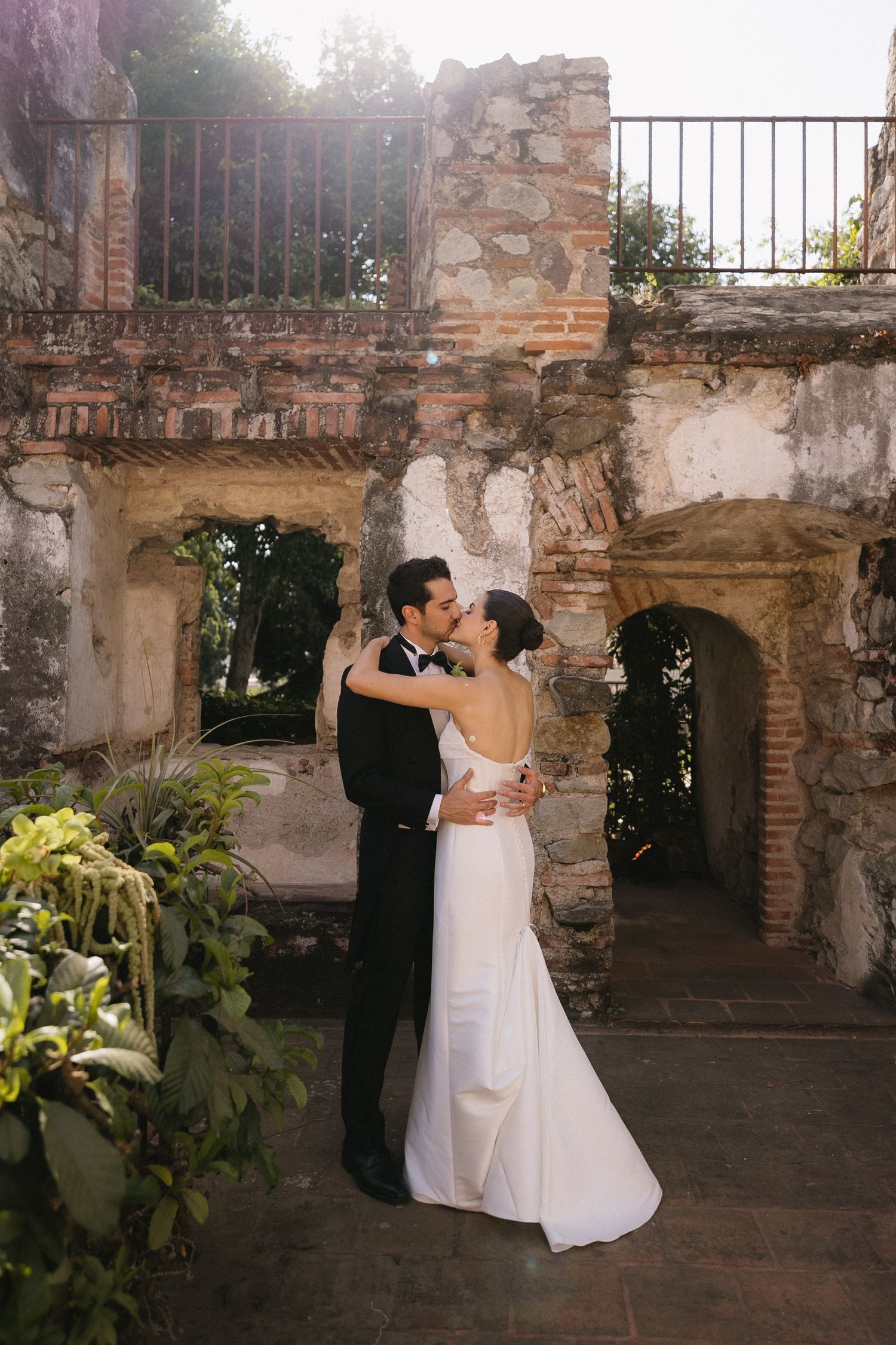Wedding couple embracing in front of rustic stone archways and greenery.