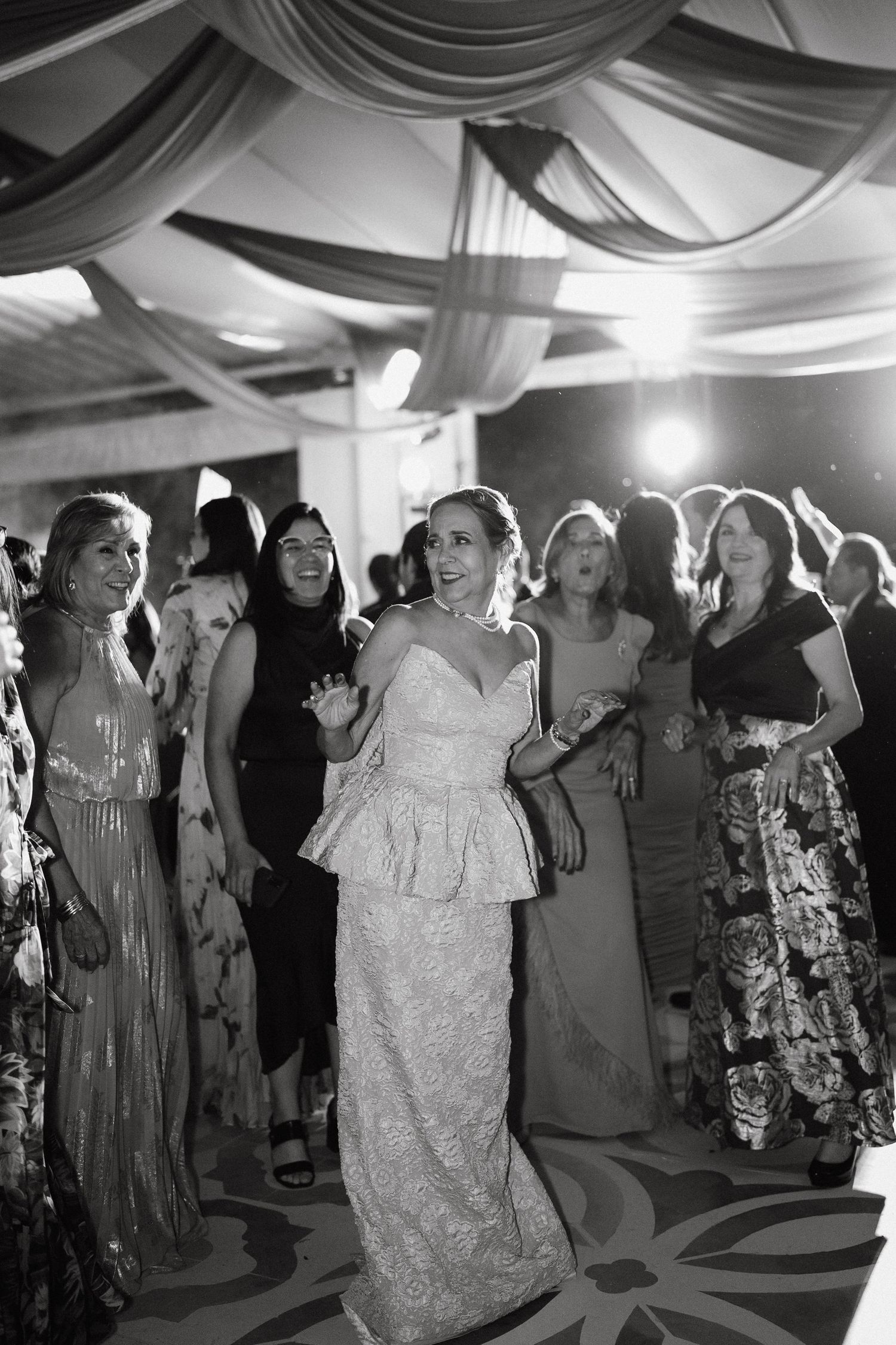 Wedding reception dance floor filled with guests celebrating under draped ceiling decor.