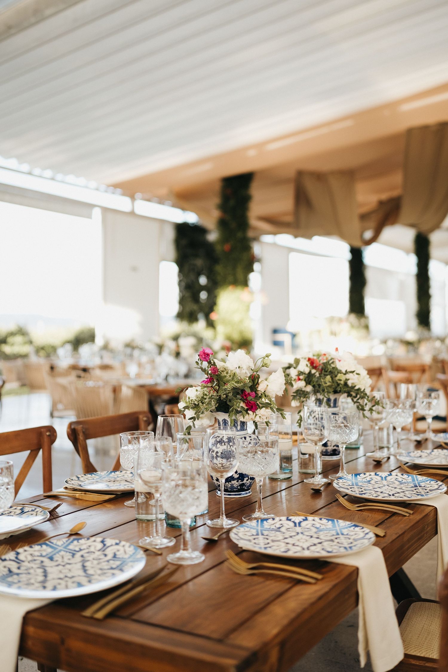 Elegant wedding reception table setting with wine glasses and wooden cross-back chairs.