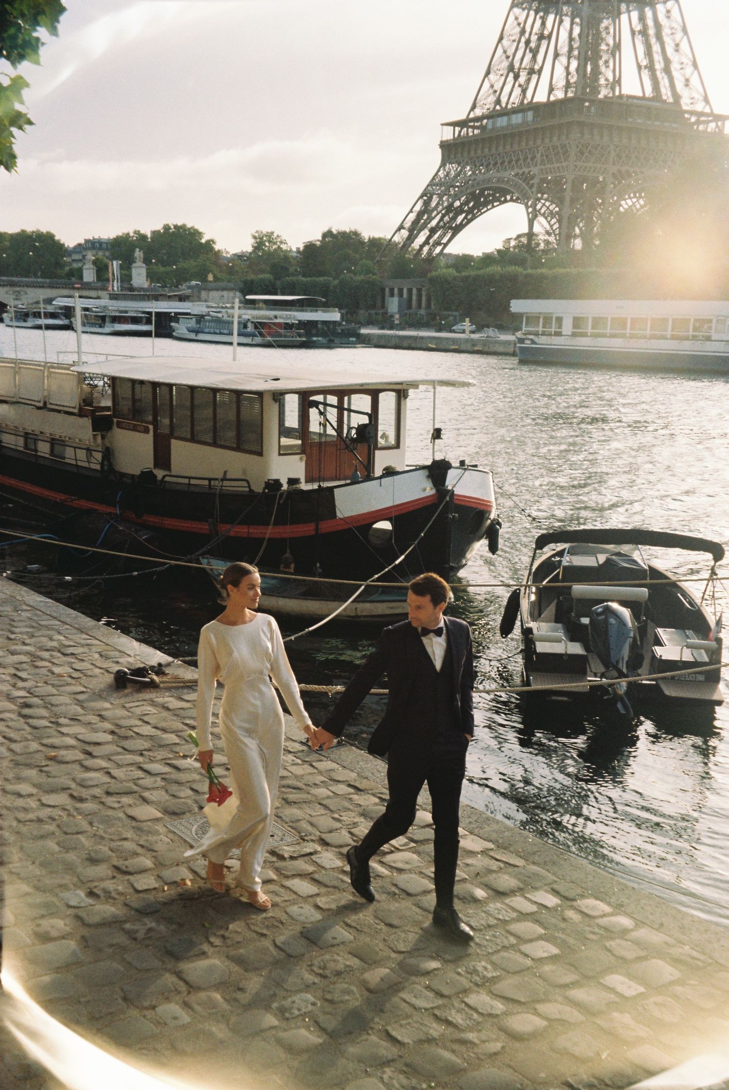 A couple walks along the Seine River cobblestone path near the Eiffel Tower in Paris during golden hour.