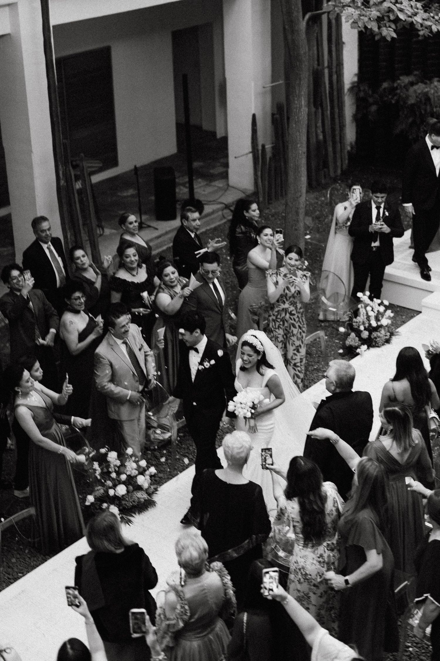 A black and white photo of wedding guests gathered in an outdoor courtyard.