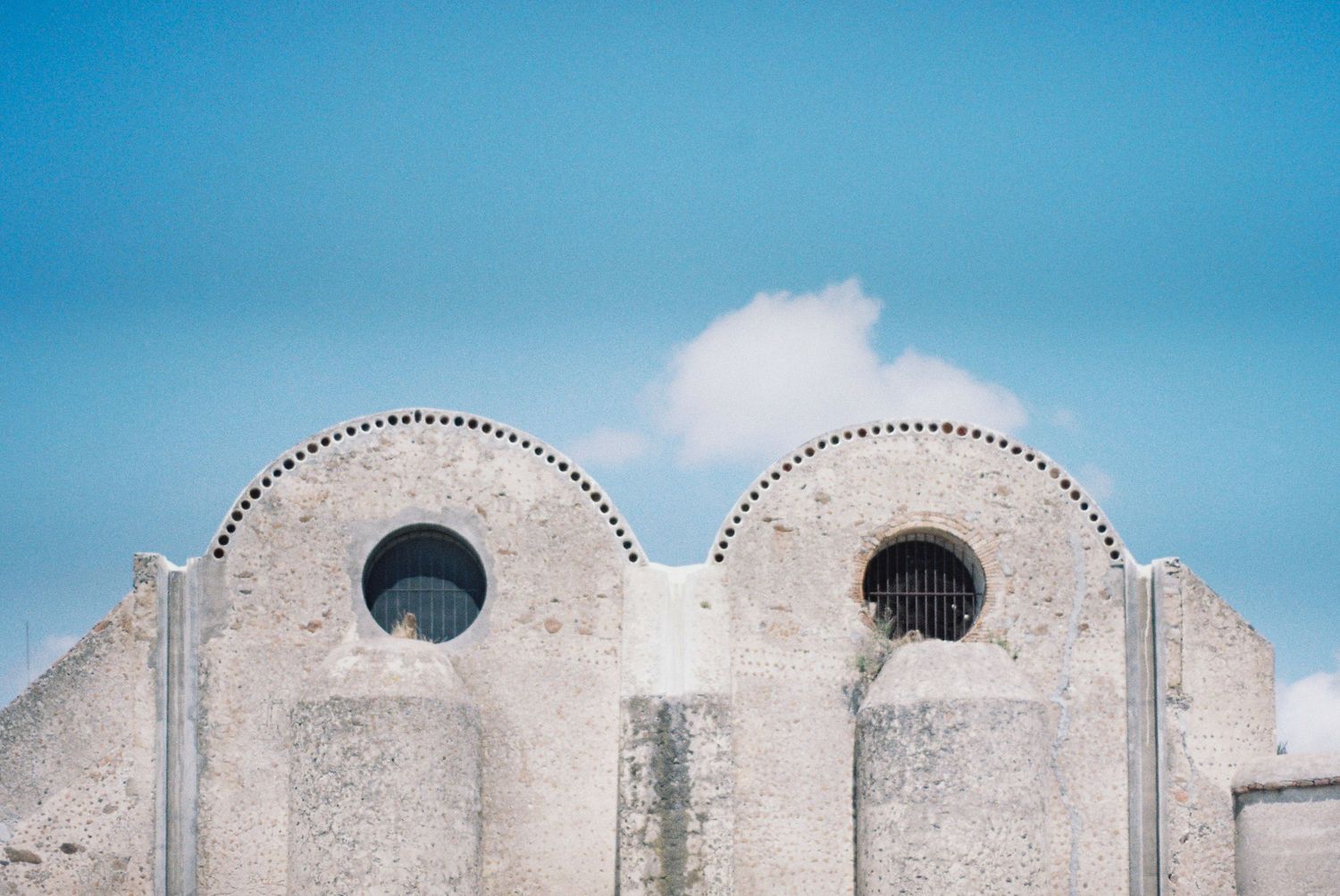 White architectural details against bright blue sky with decorative scalloped edges.