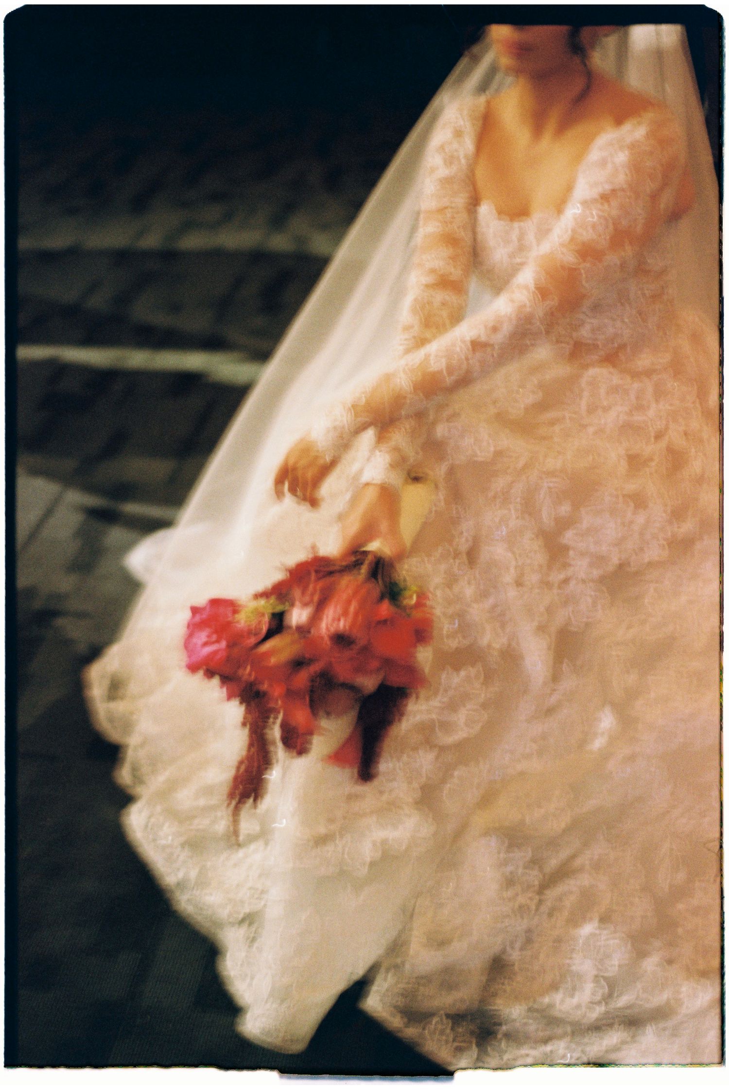 Delicate red flowers pinned to white wedding dress fabric in soft focus.