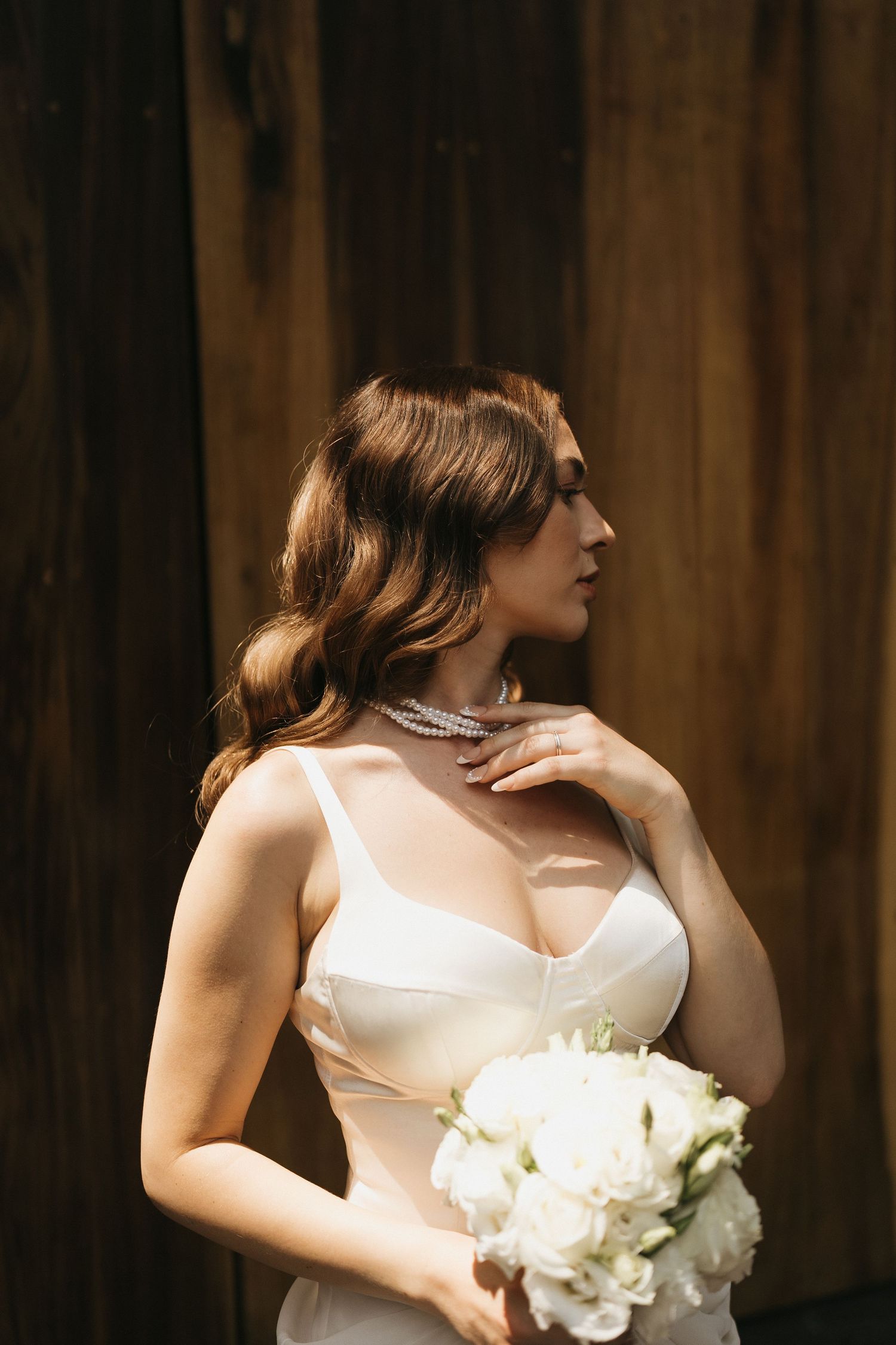 Artistic bridal portraits featuring a white dress and bouquet against wooden backdrop.
