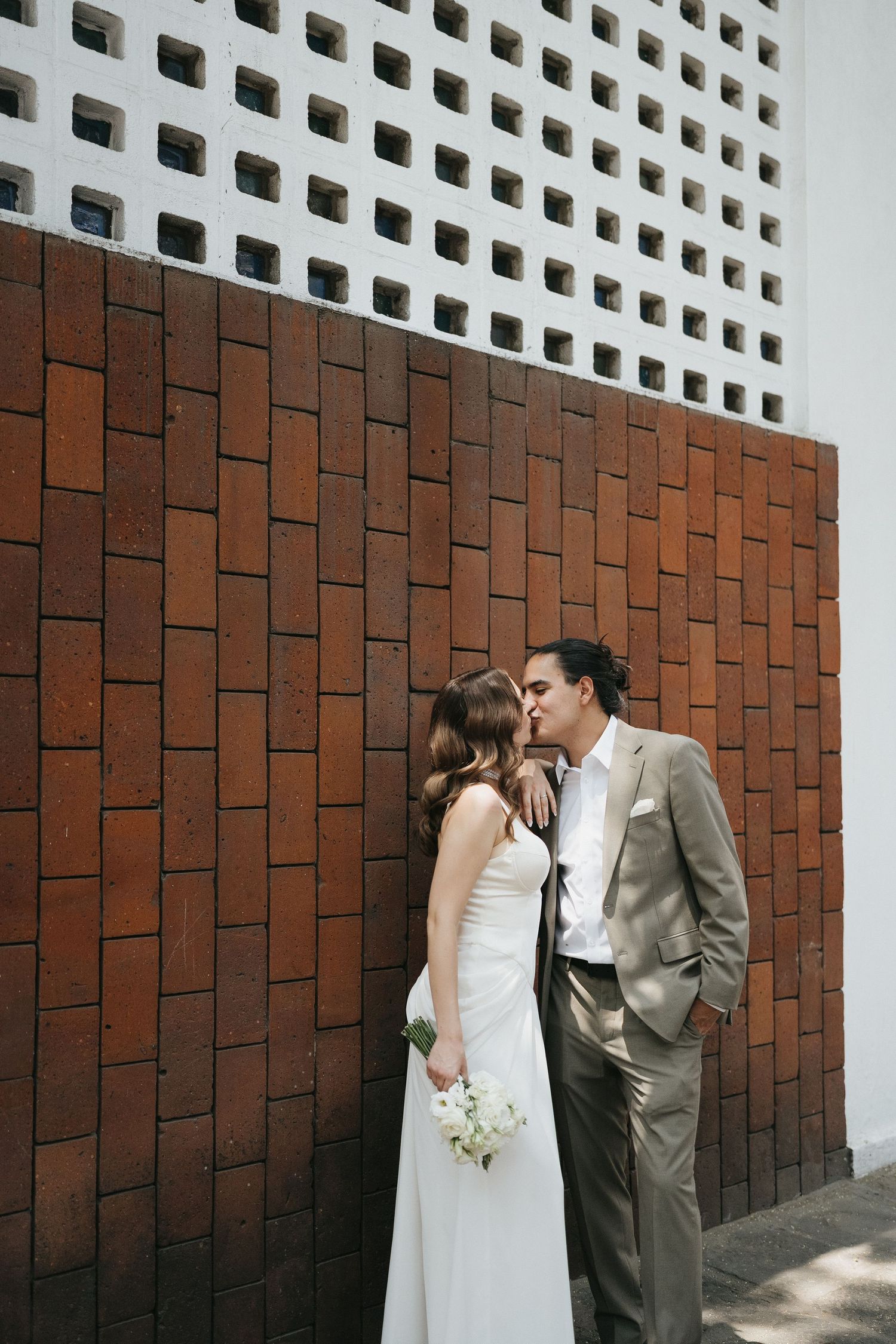 A romantic wedding moment captured against a modern brick and white lattice wall.