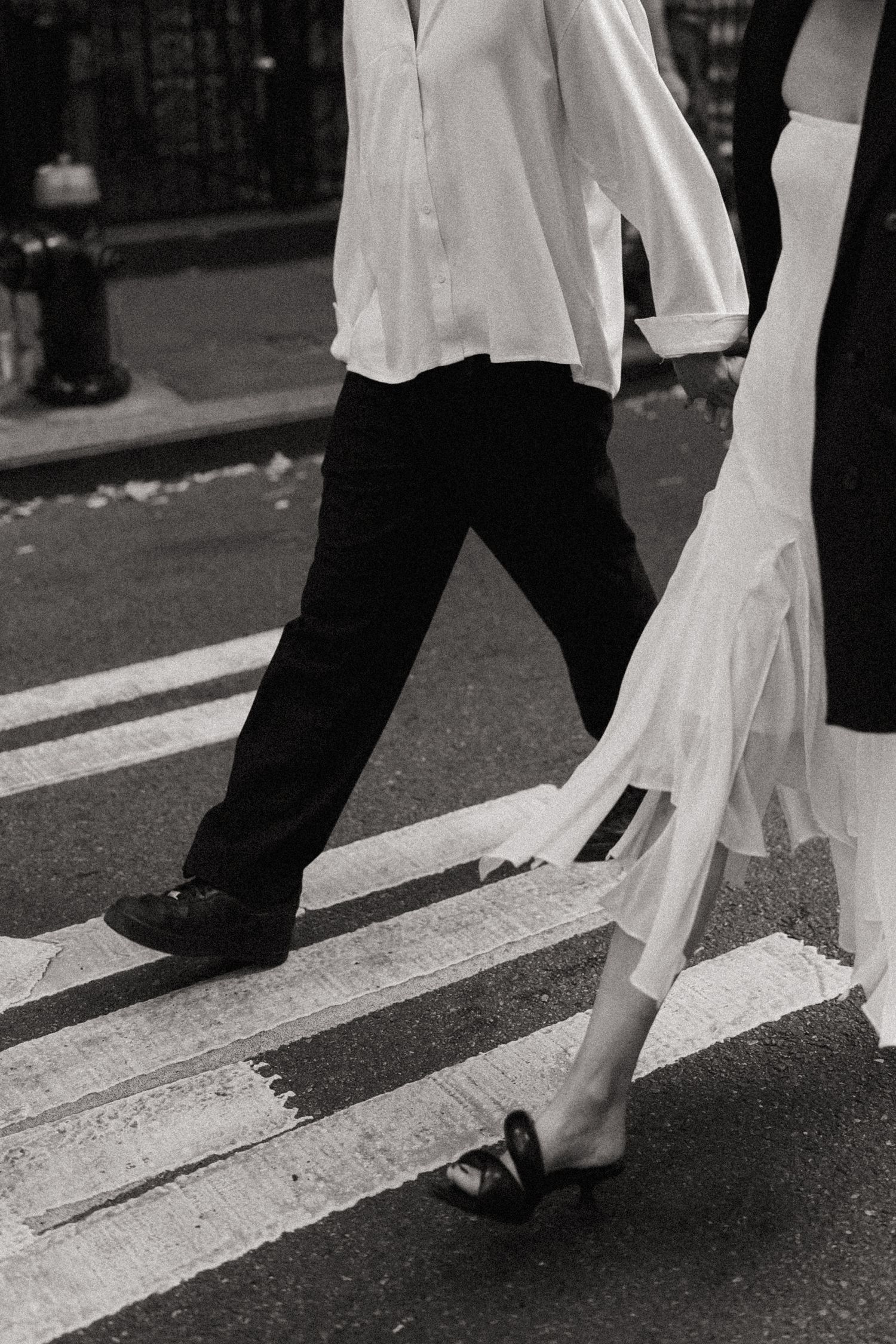 Close-up of feet crossing street showing flowing white dress and black pants.