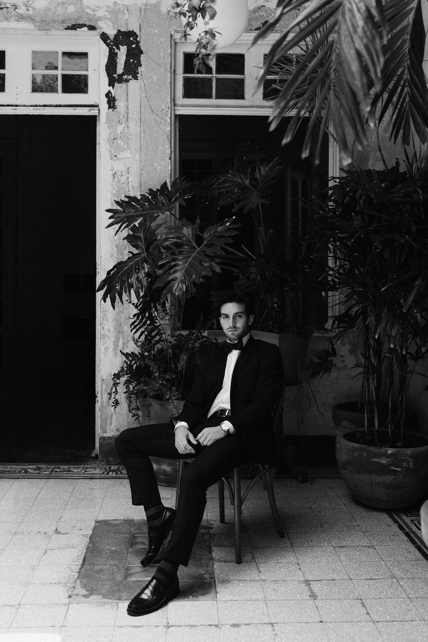 Moody black and white portraits of a person in formal attire sitting on a bench in an indoor space.