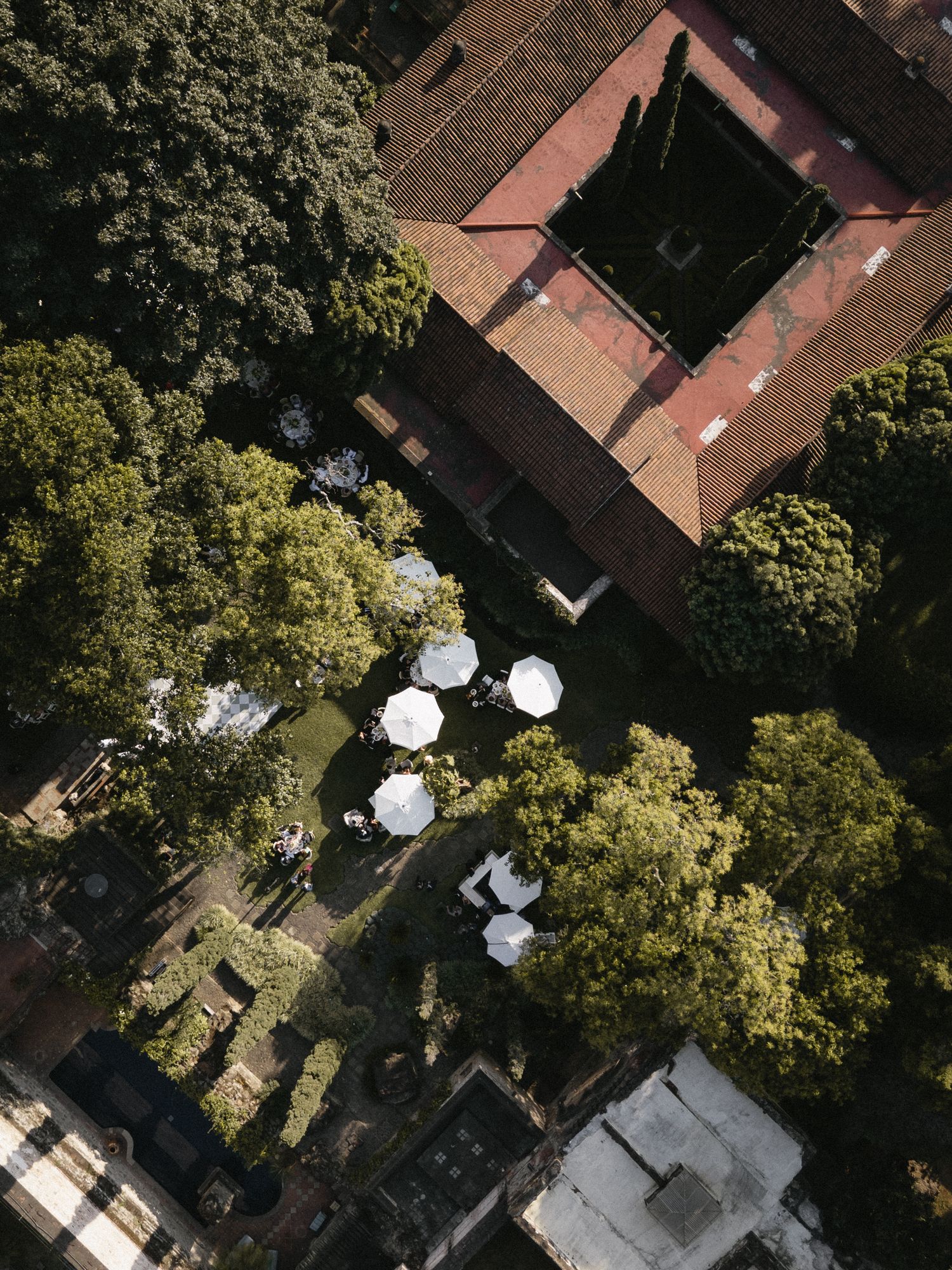 Aerial view of a historic building with white umbrellas in the courtyard surrounded by lush trees.