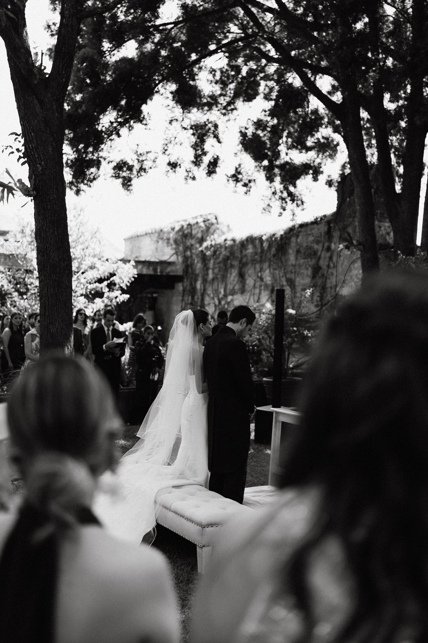 Black and white panoramic view of an outdoor wedding ceremony under trees.