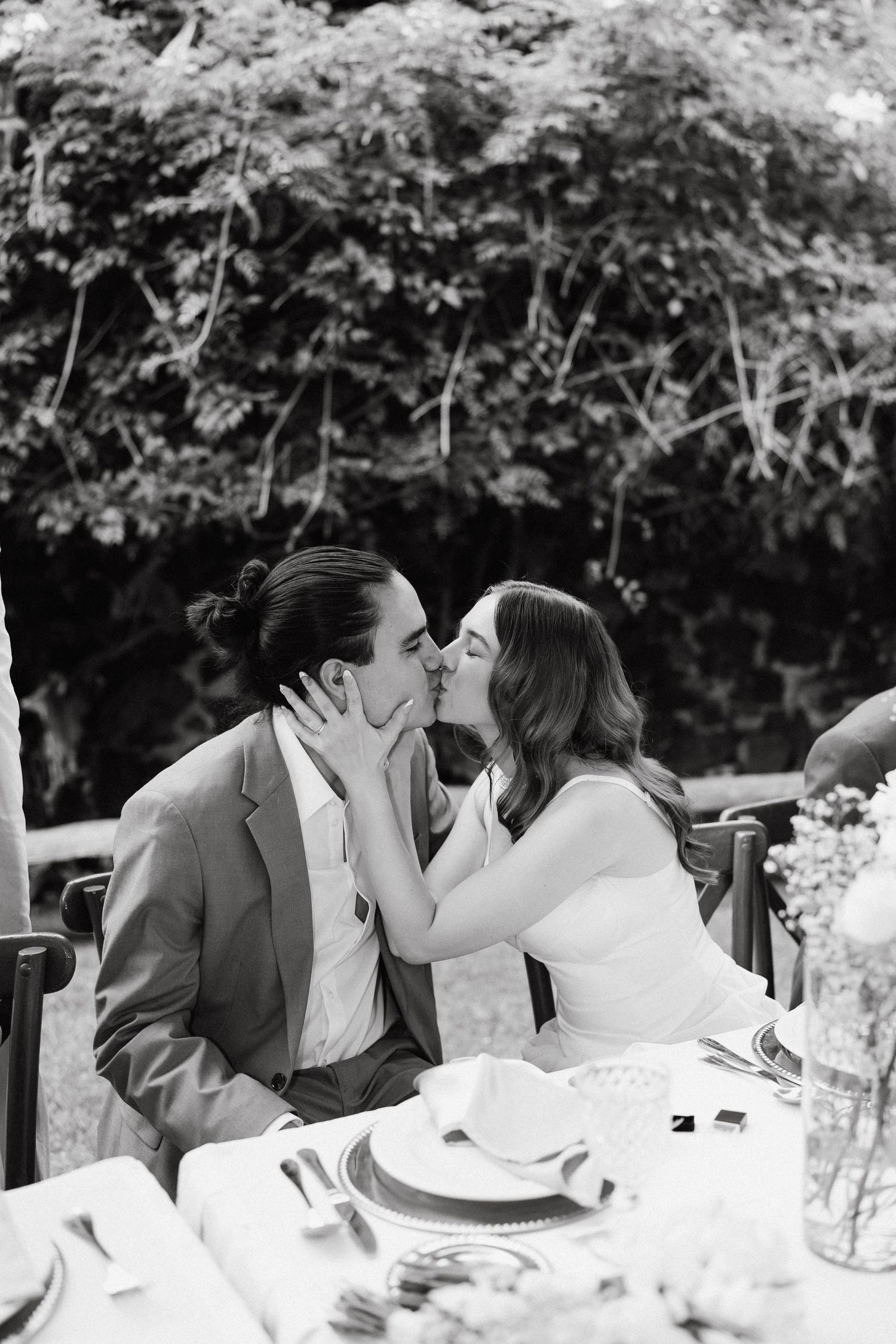 Couple shares an intimate moment at an outdoor wedding reception table with floral decorations.