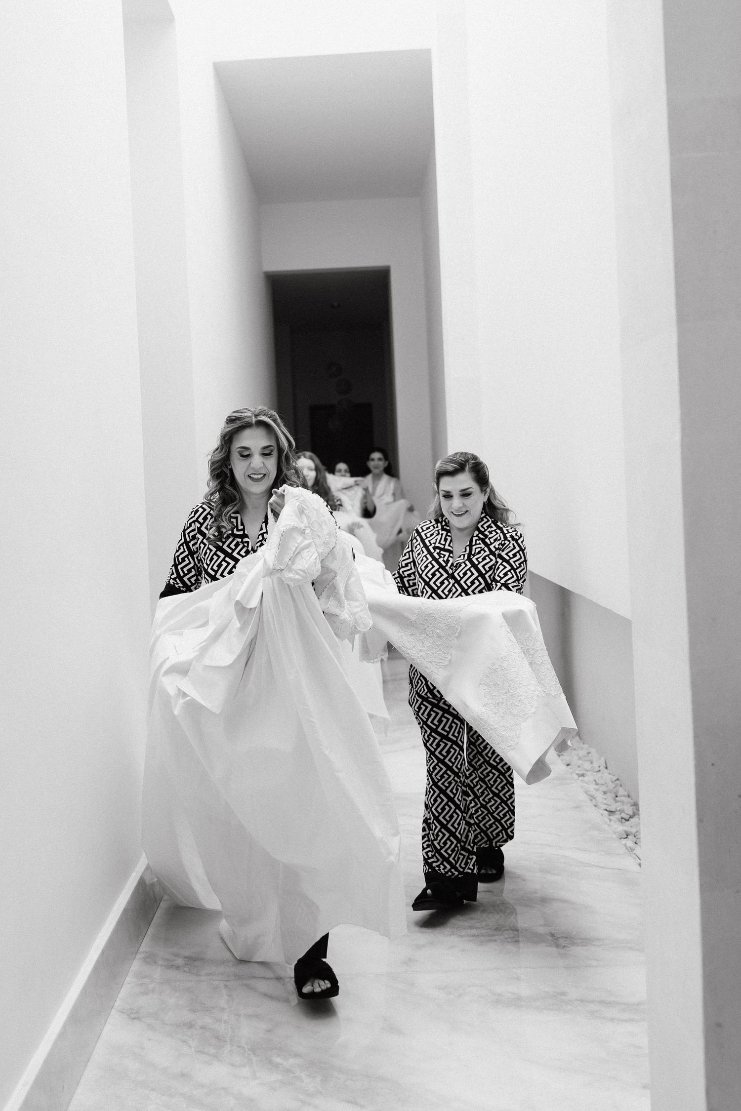 People in geometric print outfits run playfully through a modern white columned space.