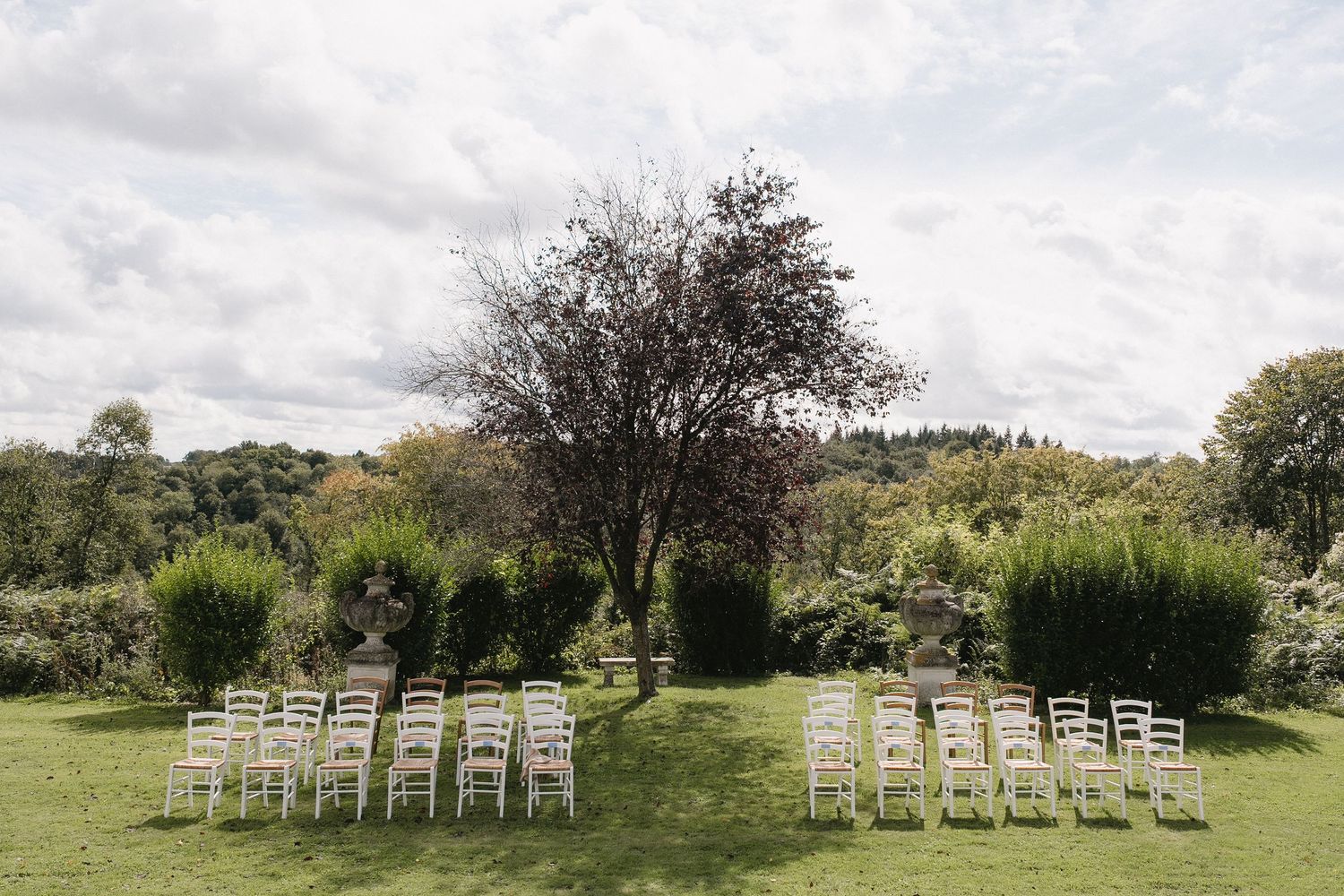 Row of white wooden chairs set up on a grassy hillside for an outdoor event.