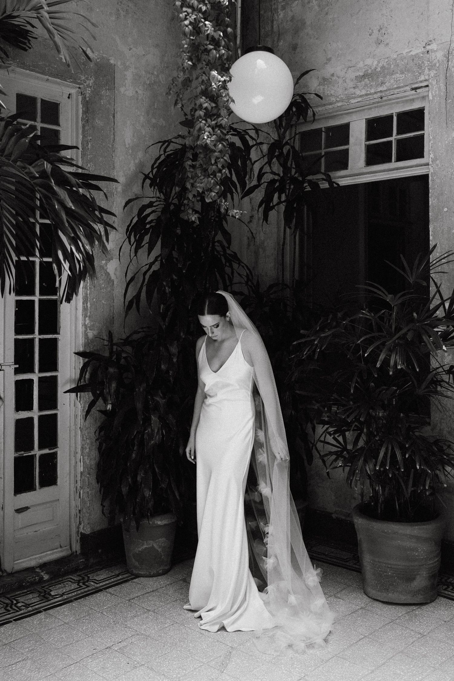 Artistic black and white photo of figures in flowing white garments among indoor plants.
