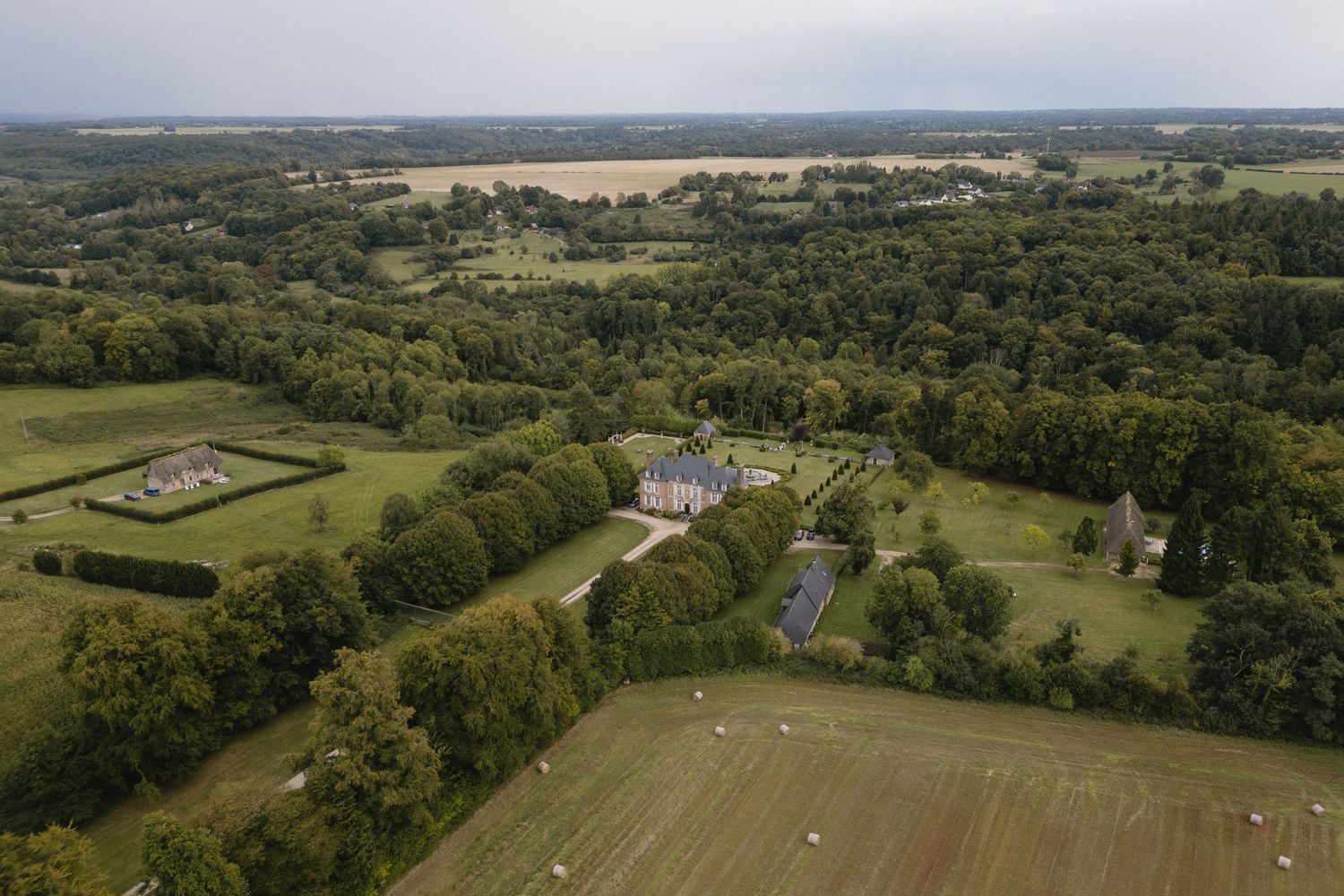 Aerial panoramic view of rolling green farmland with scattered trees and fields stretching to the horizon.