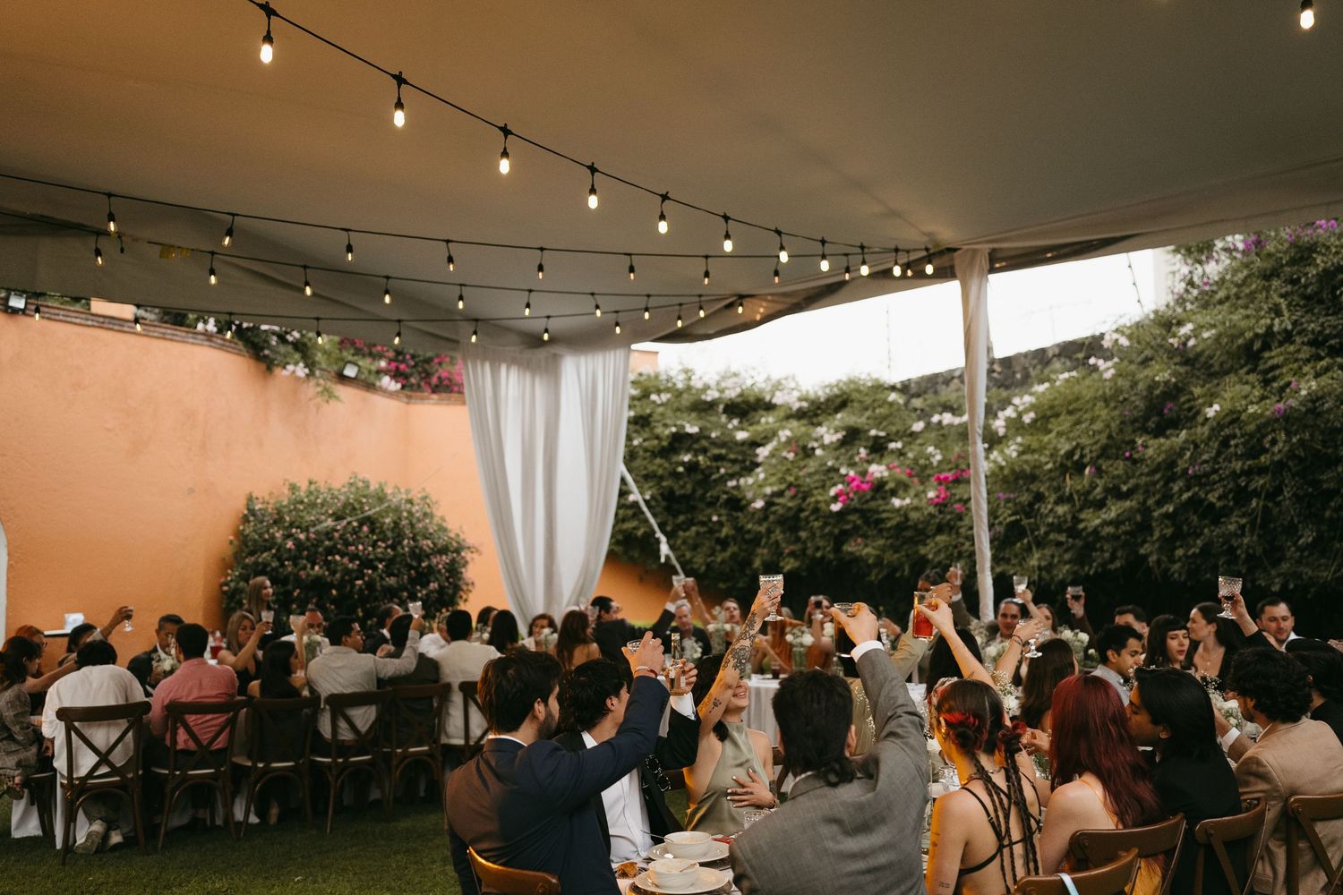 Wedding reception tent illuminated with string lights as guests gather for evening celebrations.
