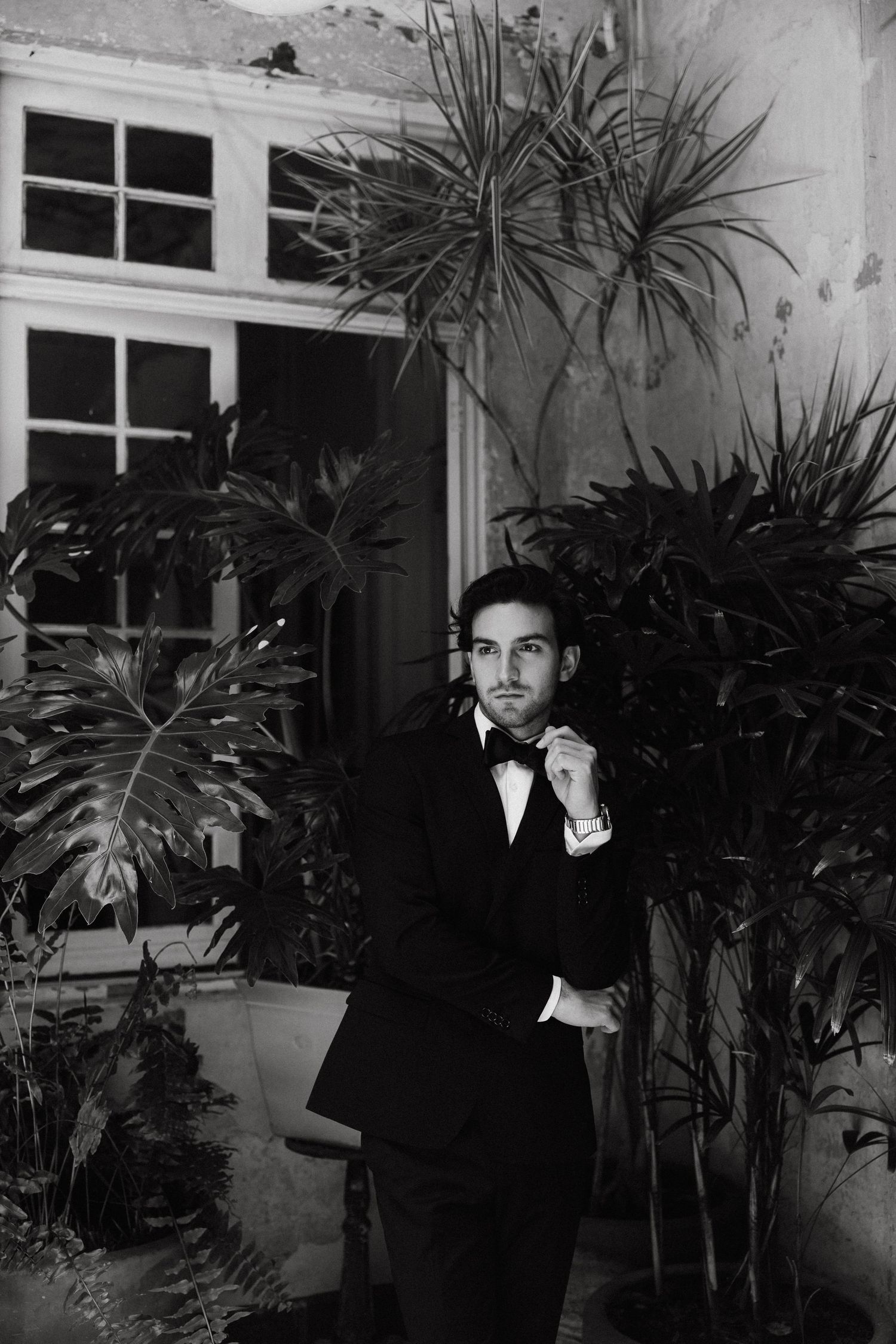 Black and white portrait in formal attire against a backdrop of tropical plants.