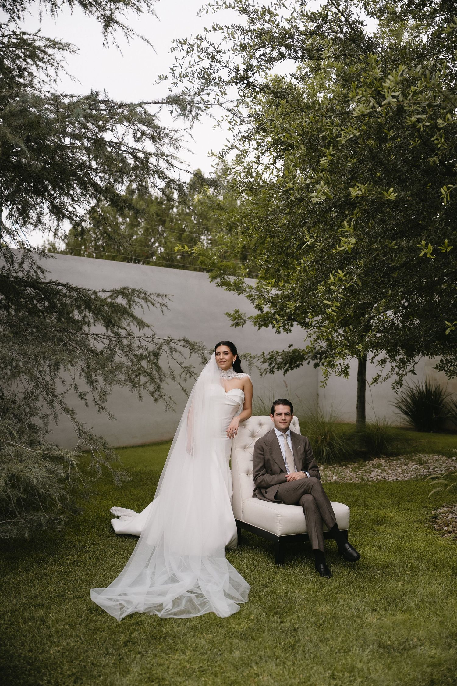 Wedding couple posing on grass with trees in background during outdoor photo session.