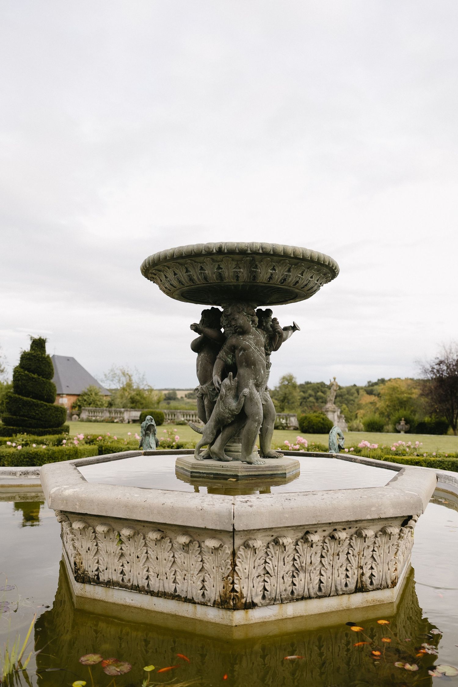 Ornate stone fountain with carved figures and decorative basin in a formal garden setting.