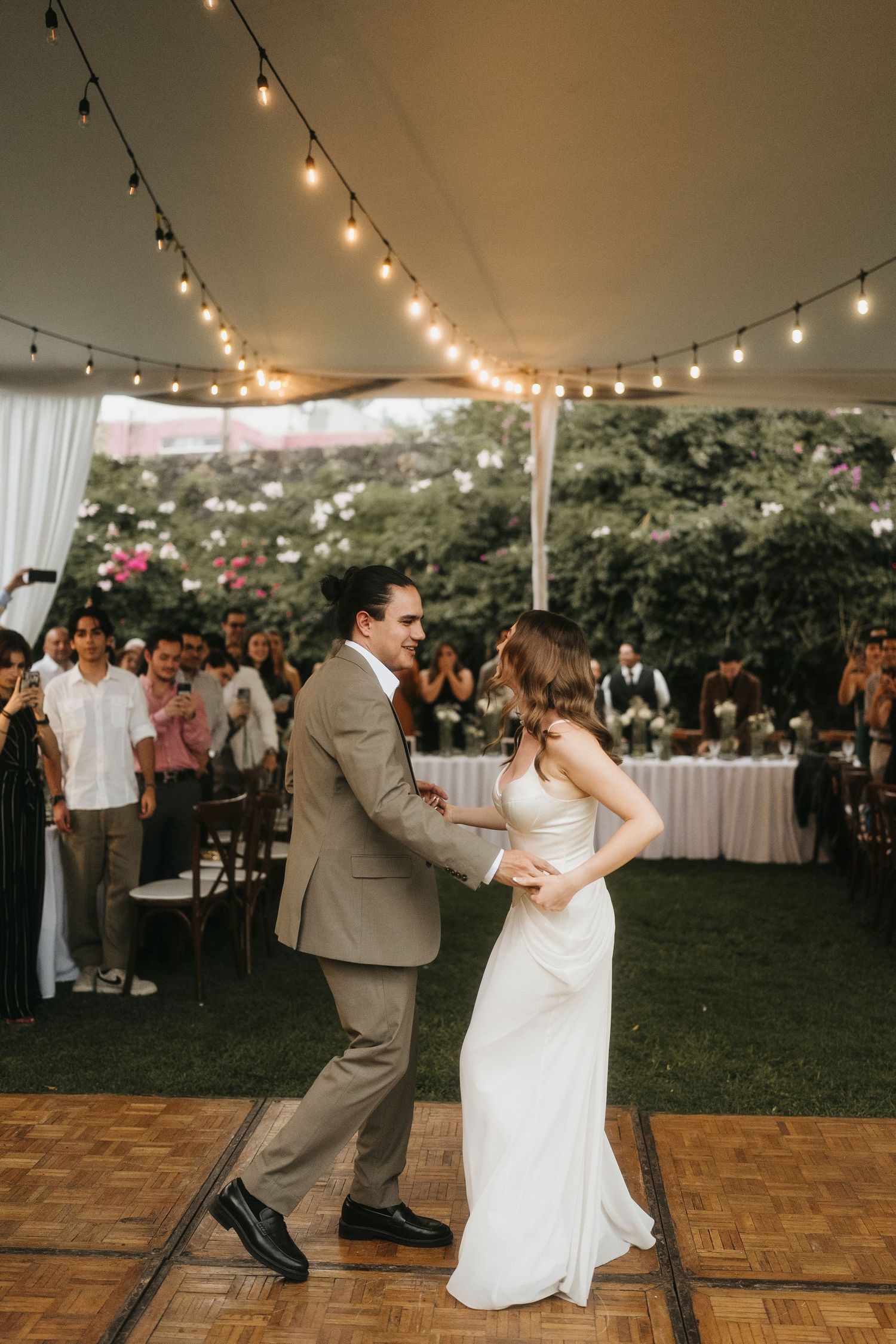 Couple performs a choreographed dance routine on a wooden dance floor under a tent with string lights.