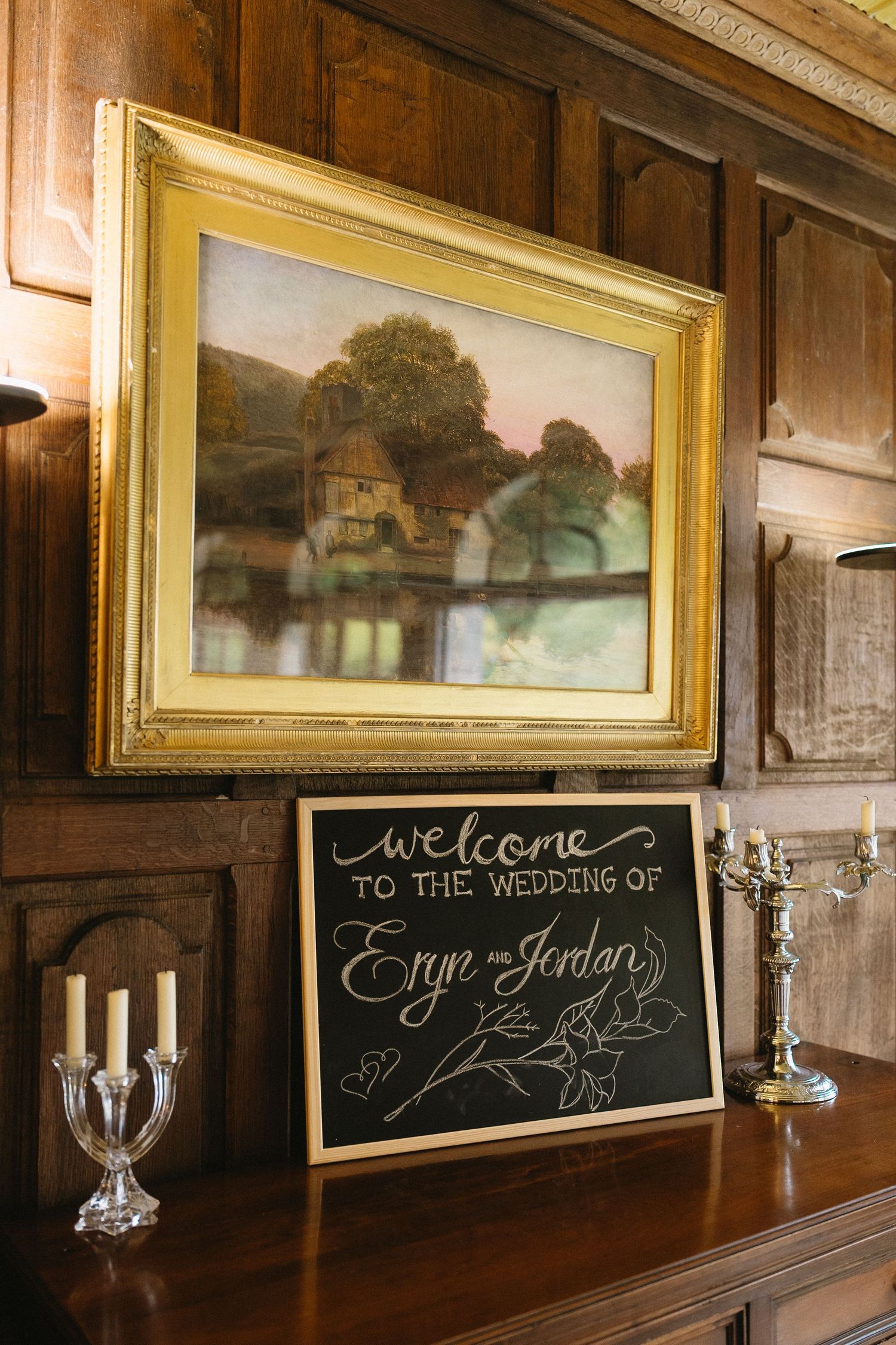 Rustic wooden wall with vintage paintings and chalkboard signs displaying wedding welcome messages.