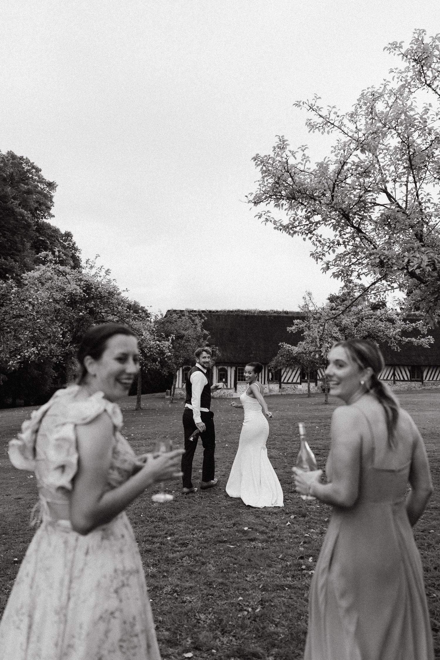 Wedding party members share laughs together on a grassy field during celebrations.