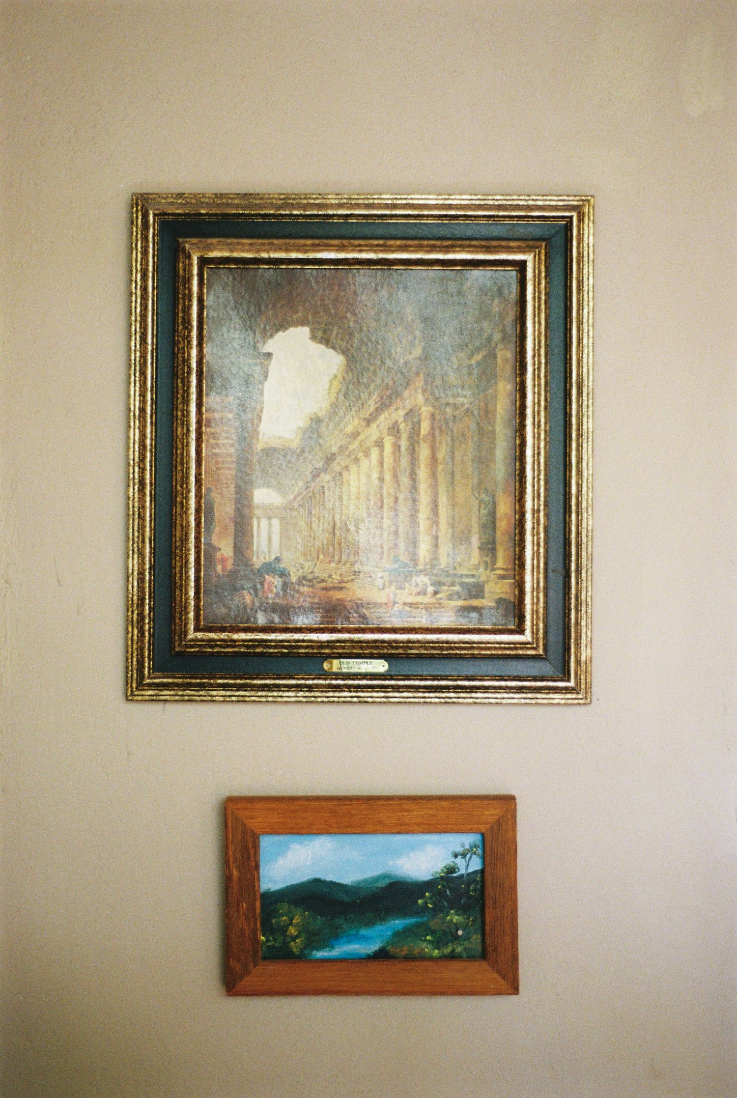 Two framed artworks on wall - classical columns above and landscape scene below.