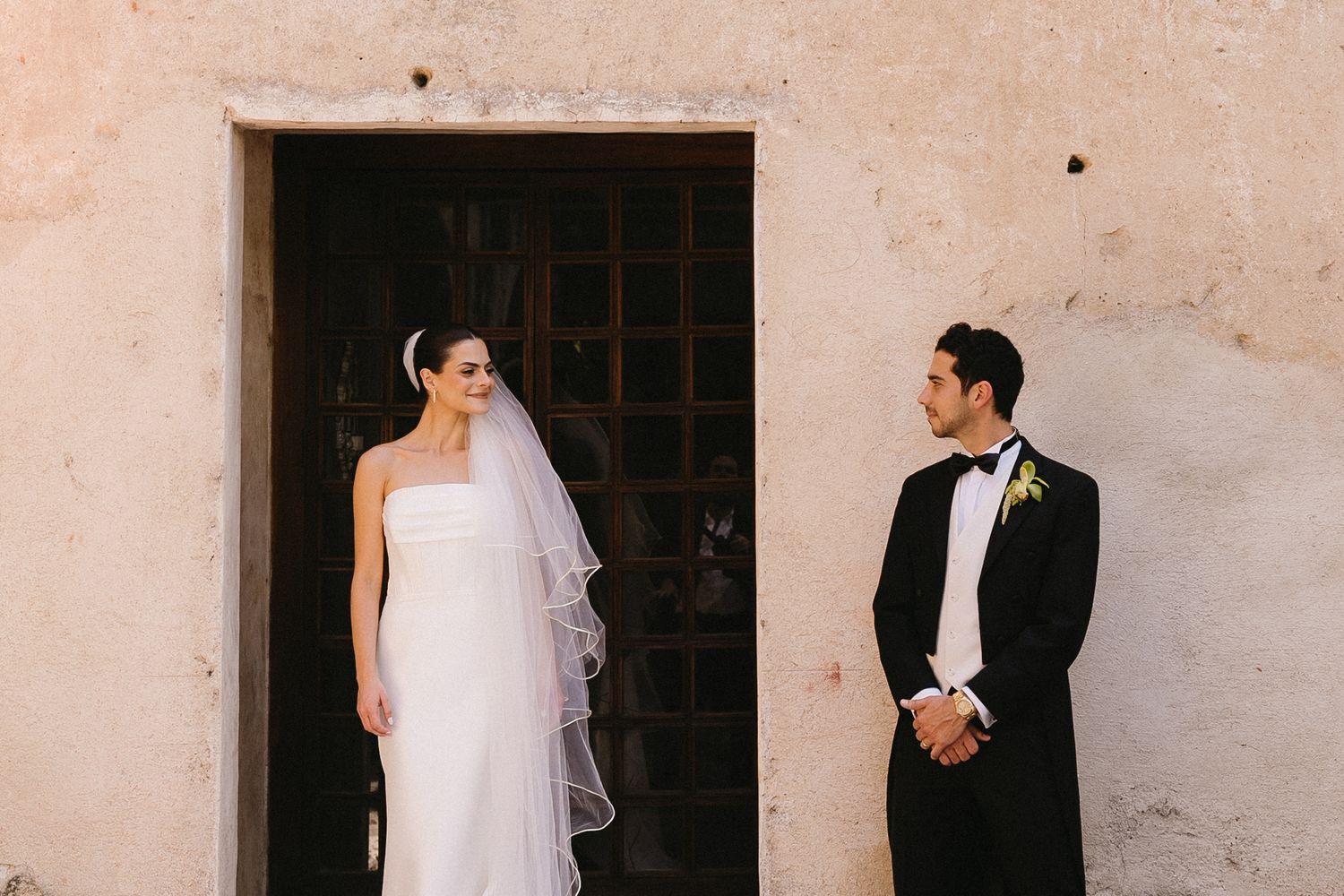 Wedding couple photographed against a light stone wall in an elegant outdoor setting.
