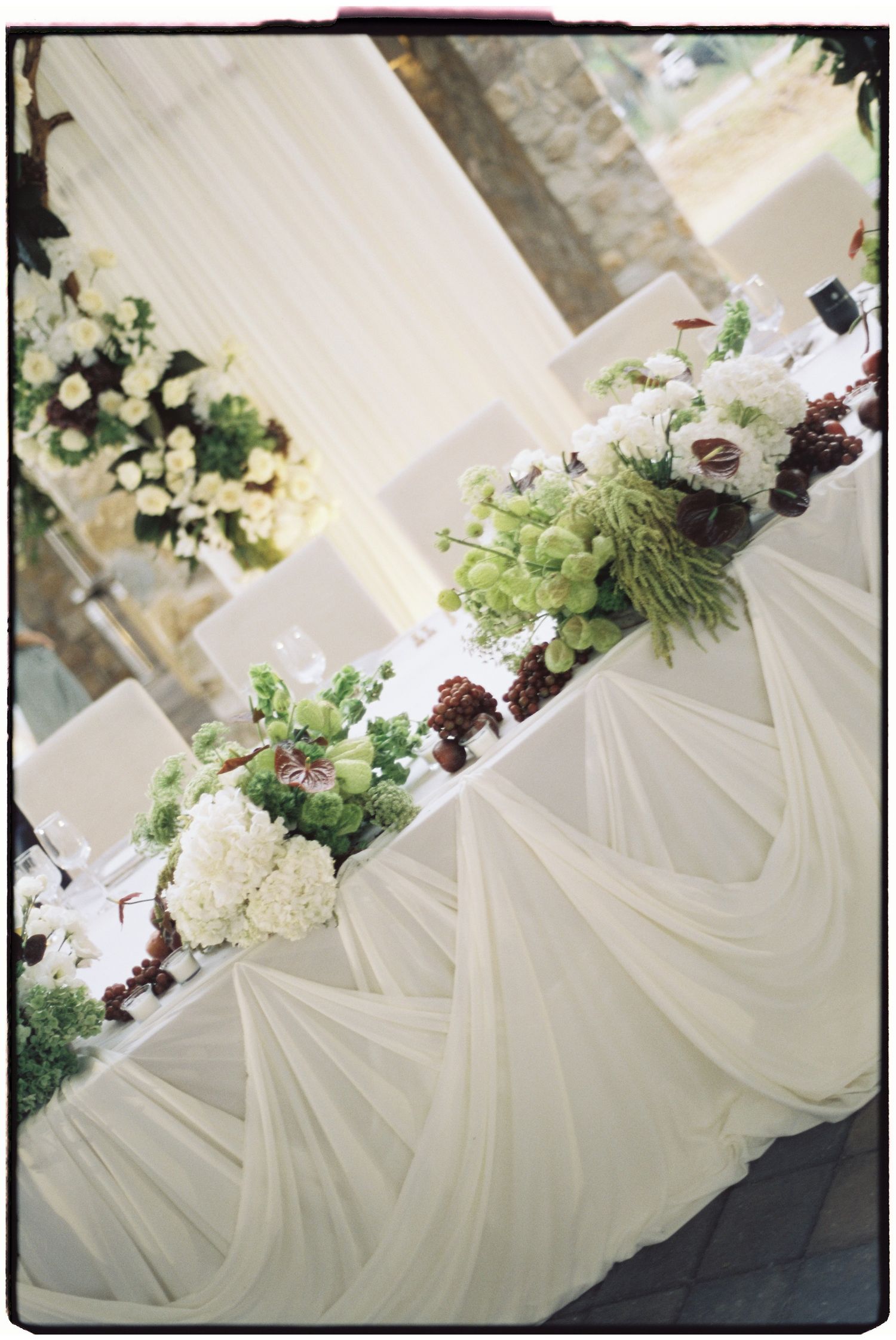 Elegant white tablecloth reception decor with floral arrangements and greenery.