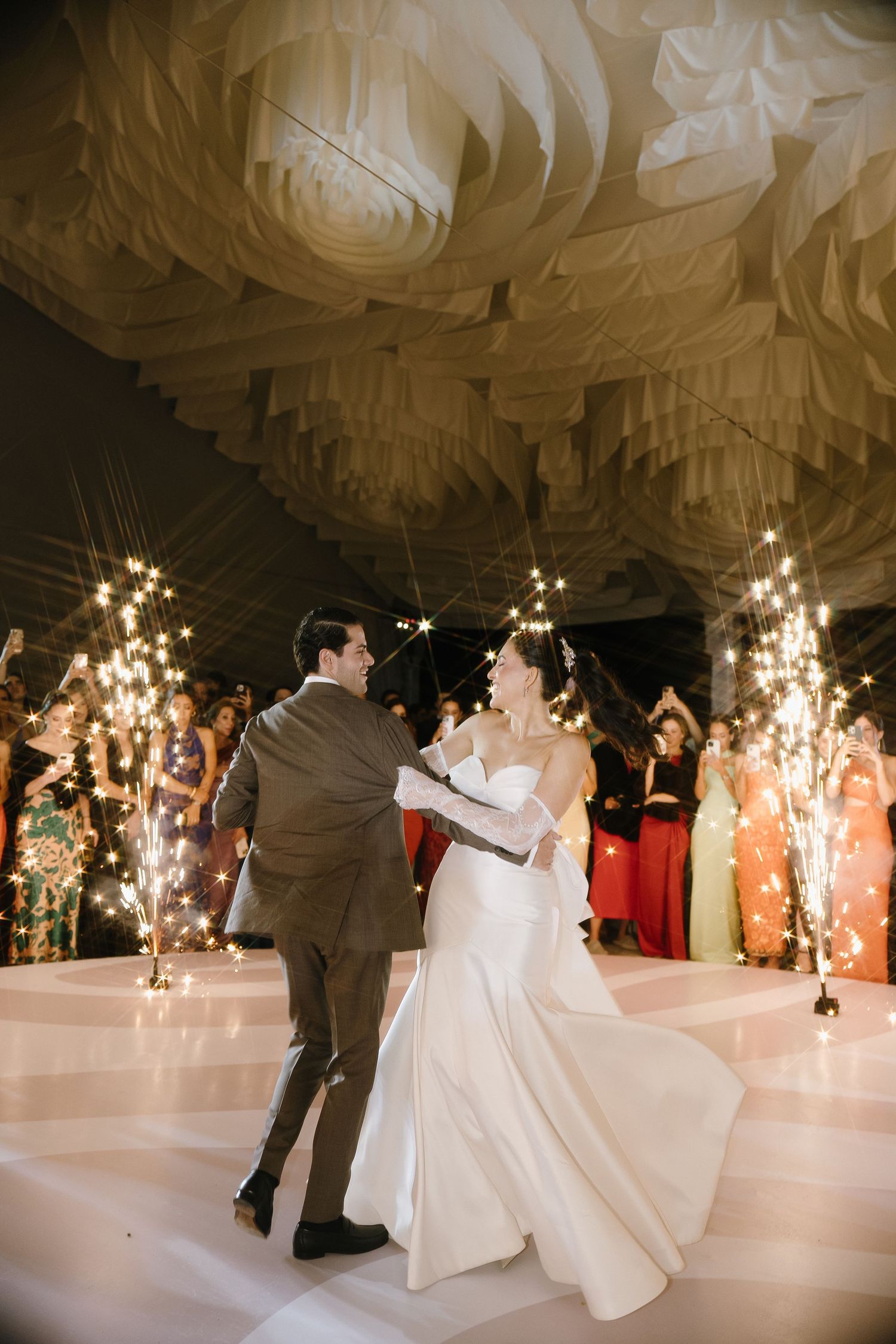 A couple shares their first dance under elegant draped fabric ceiling with sparkler effects.