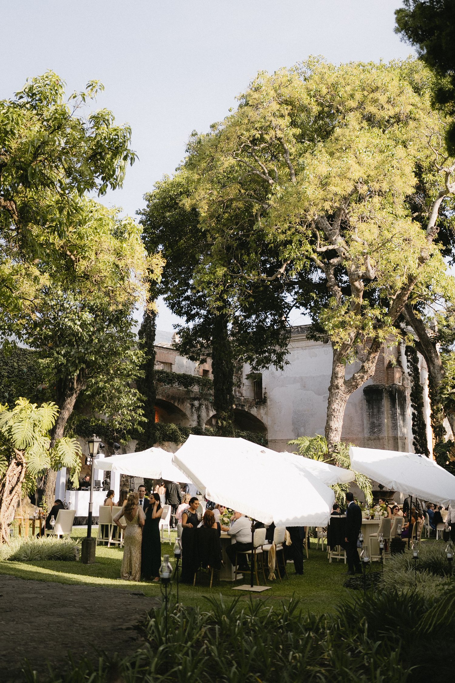 Outdoor wedding reception setup with white tents and mature trees.