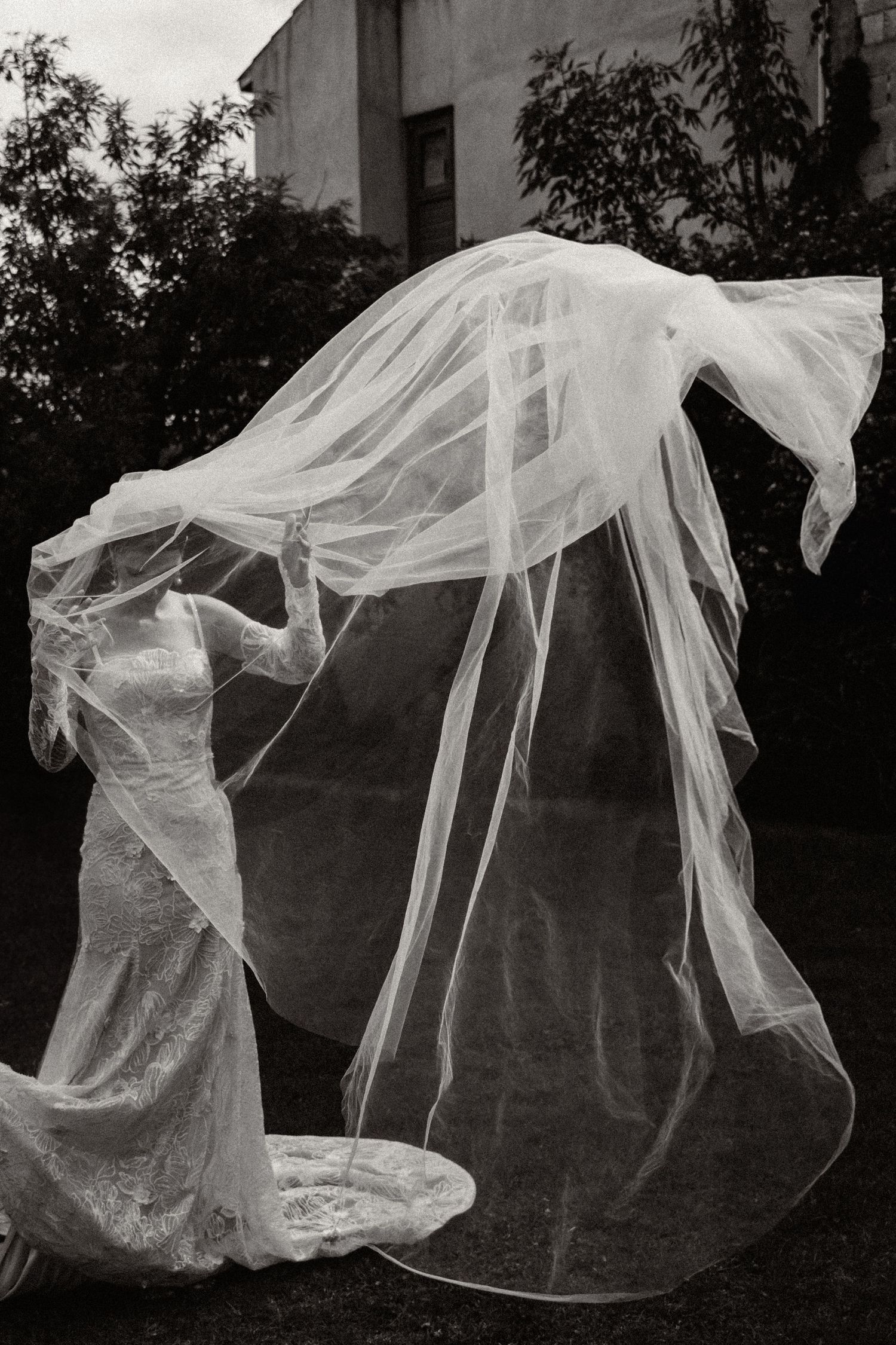 A flowing white veil and dress create an ethereal silhouette against a dark background in this artistic black and white photo.