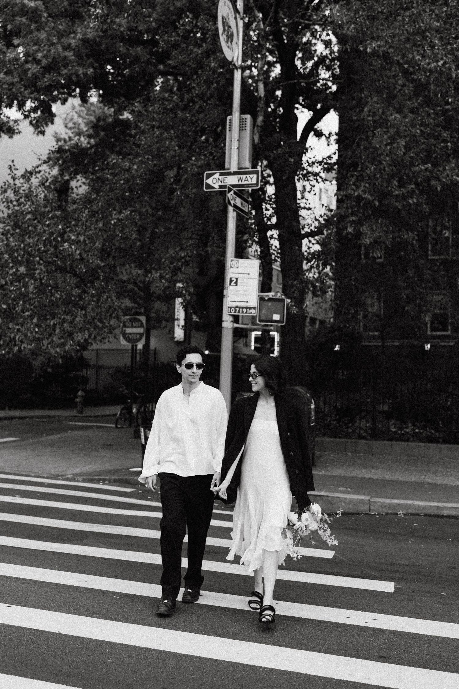Couple walking across a crosswalk on a tree-lined street.