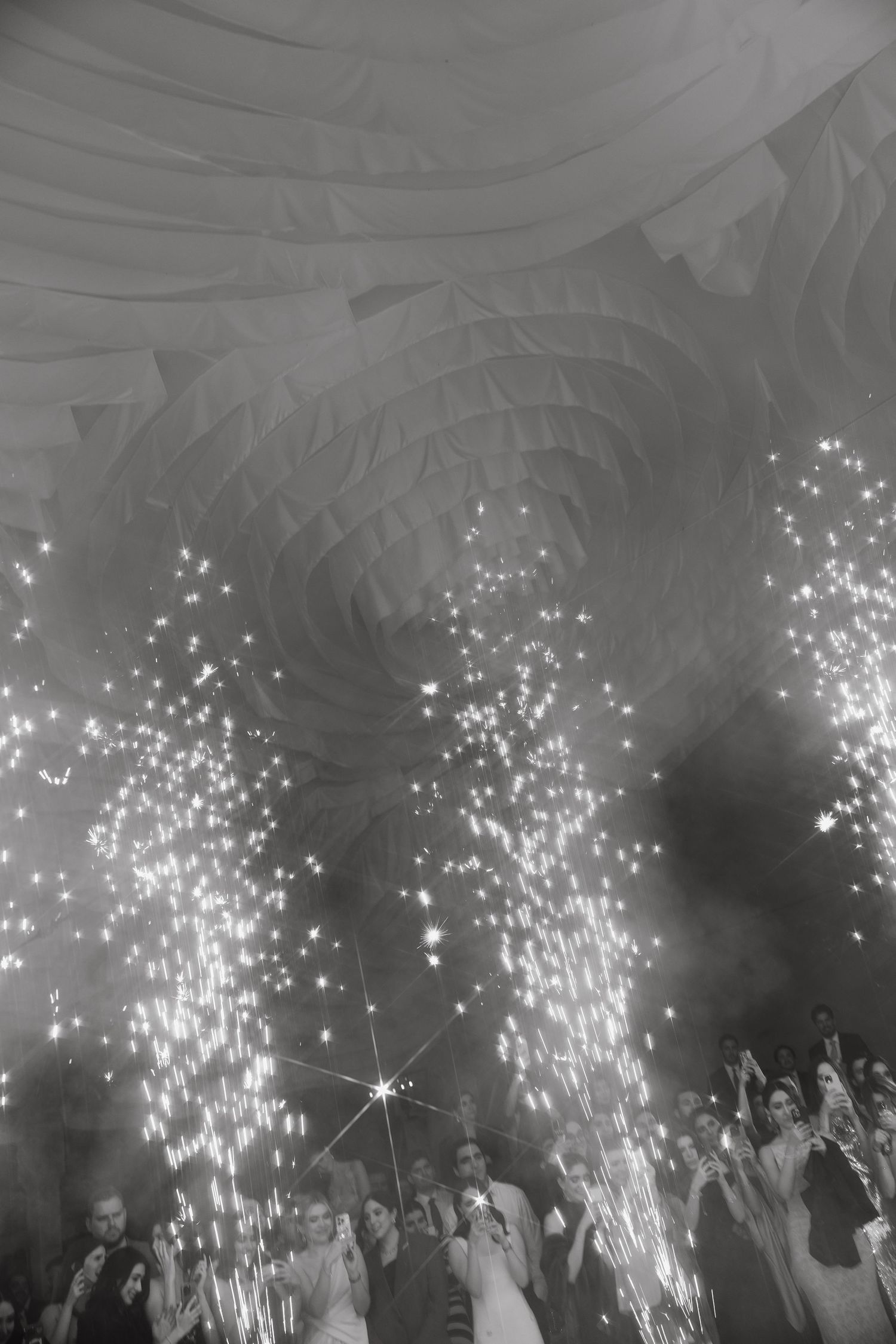 Indoor wedding celebration with sparklers creating magical light streams under draped ceiling.