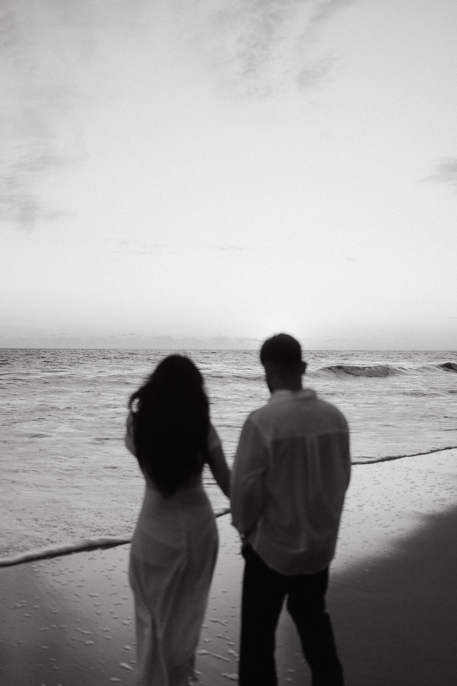 Silhouettes walking along a beach at sunset in black and white.