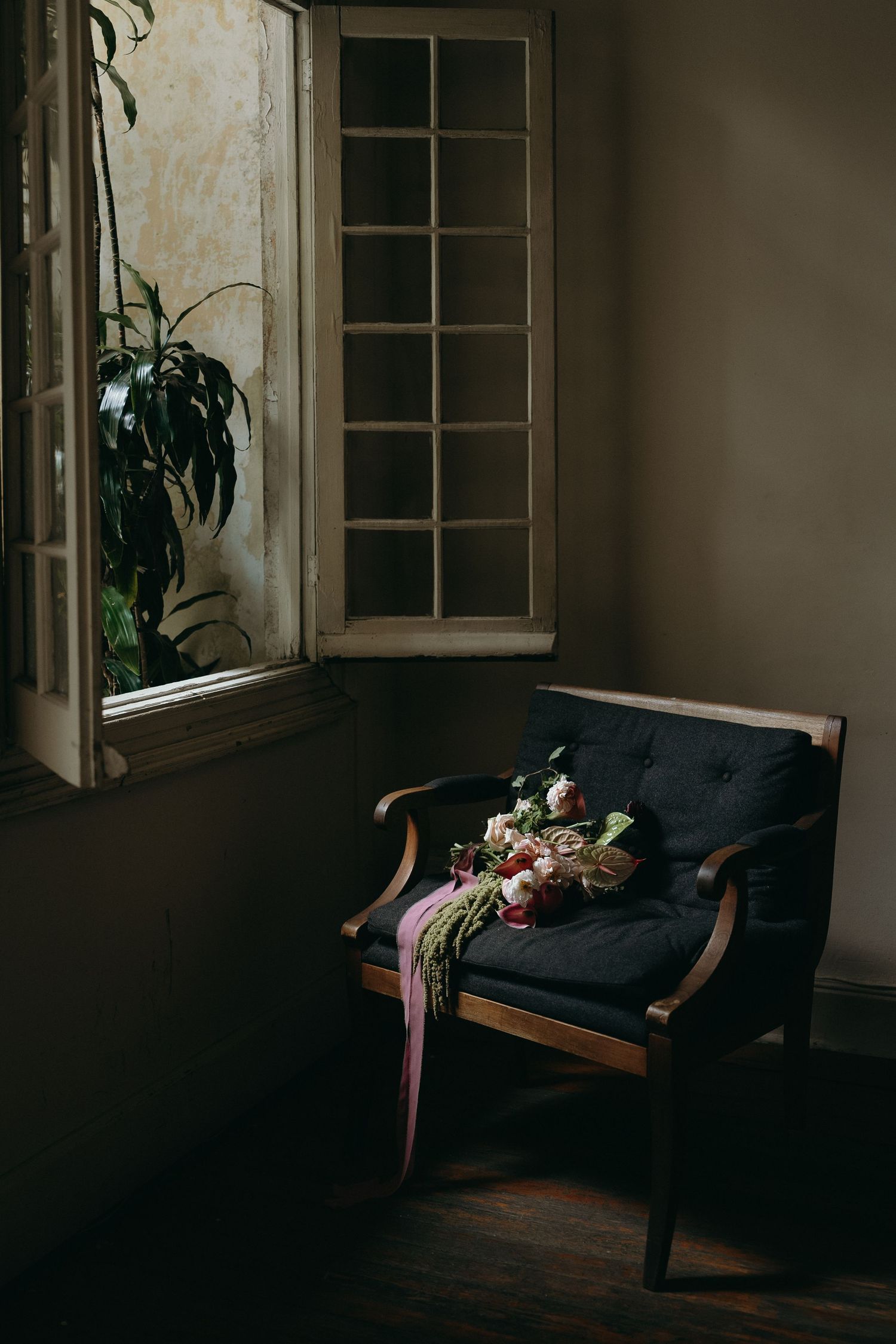 A dark moody room with a black couch and floral arrangement by a window.