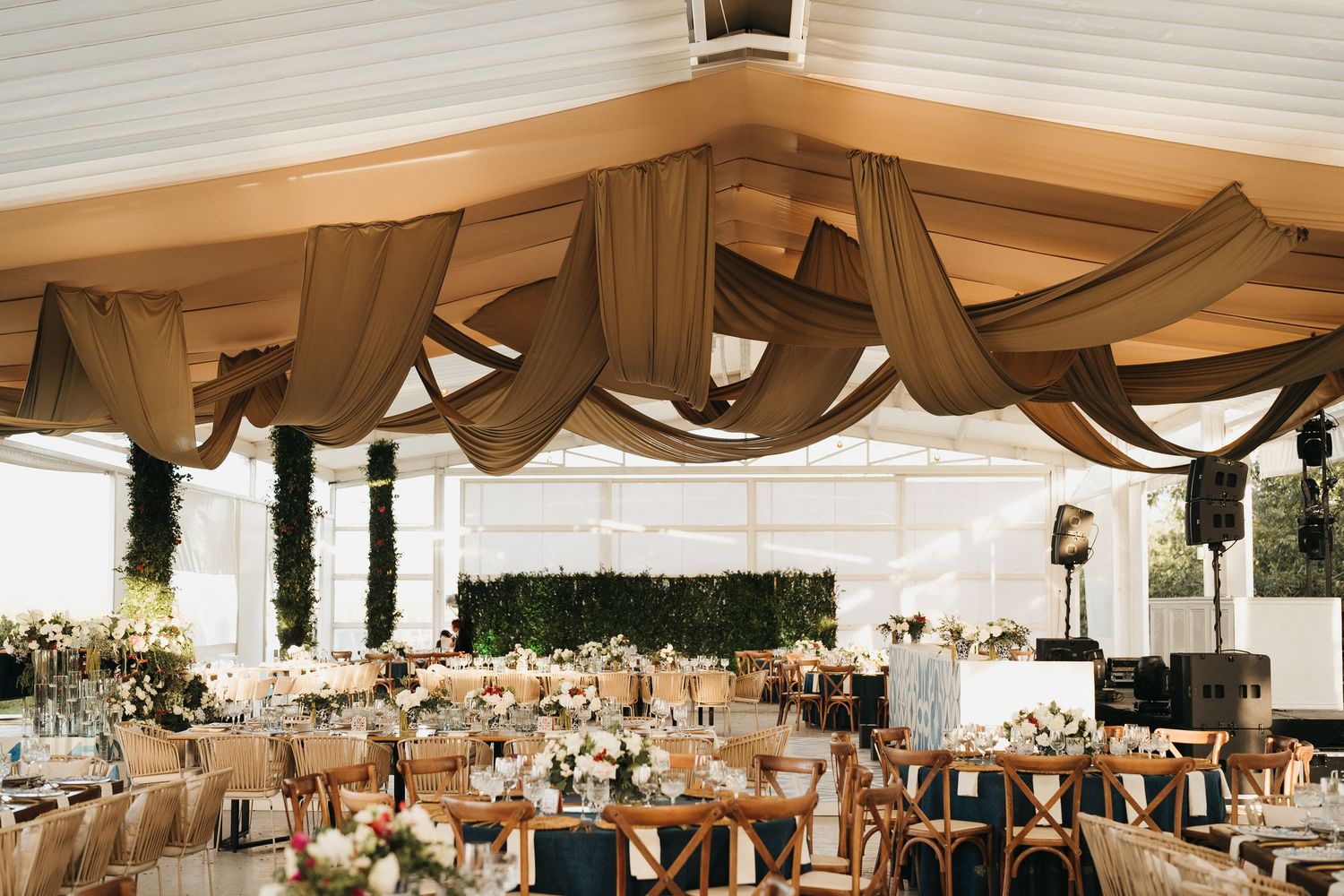 An elegant wedding reception venue with draped fabric ceiling and long dining tables.