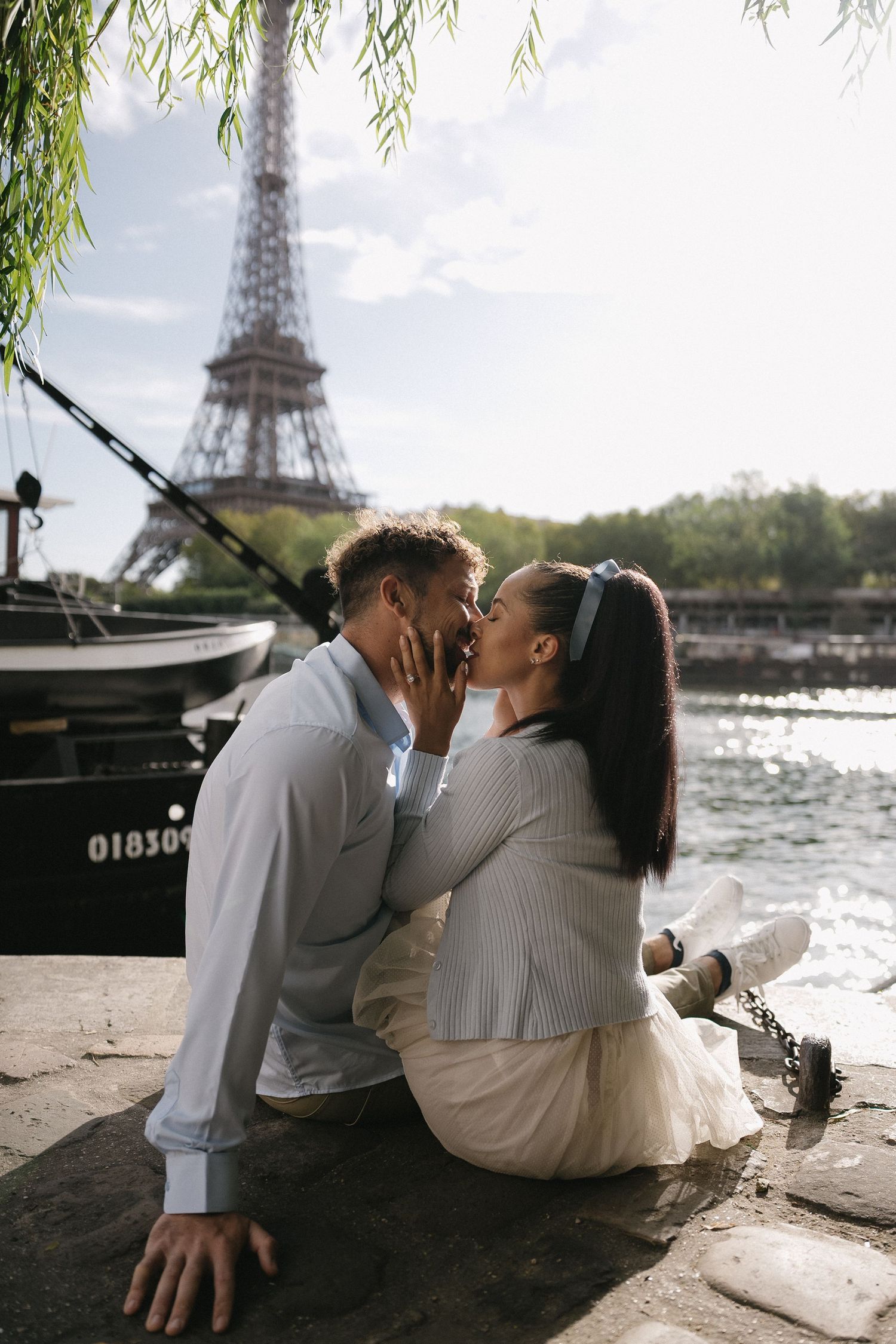 Romantic couple sitting by the Seine River with Eiffel Tower in background.