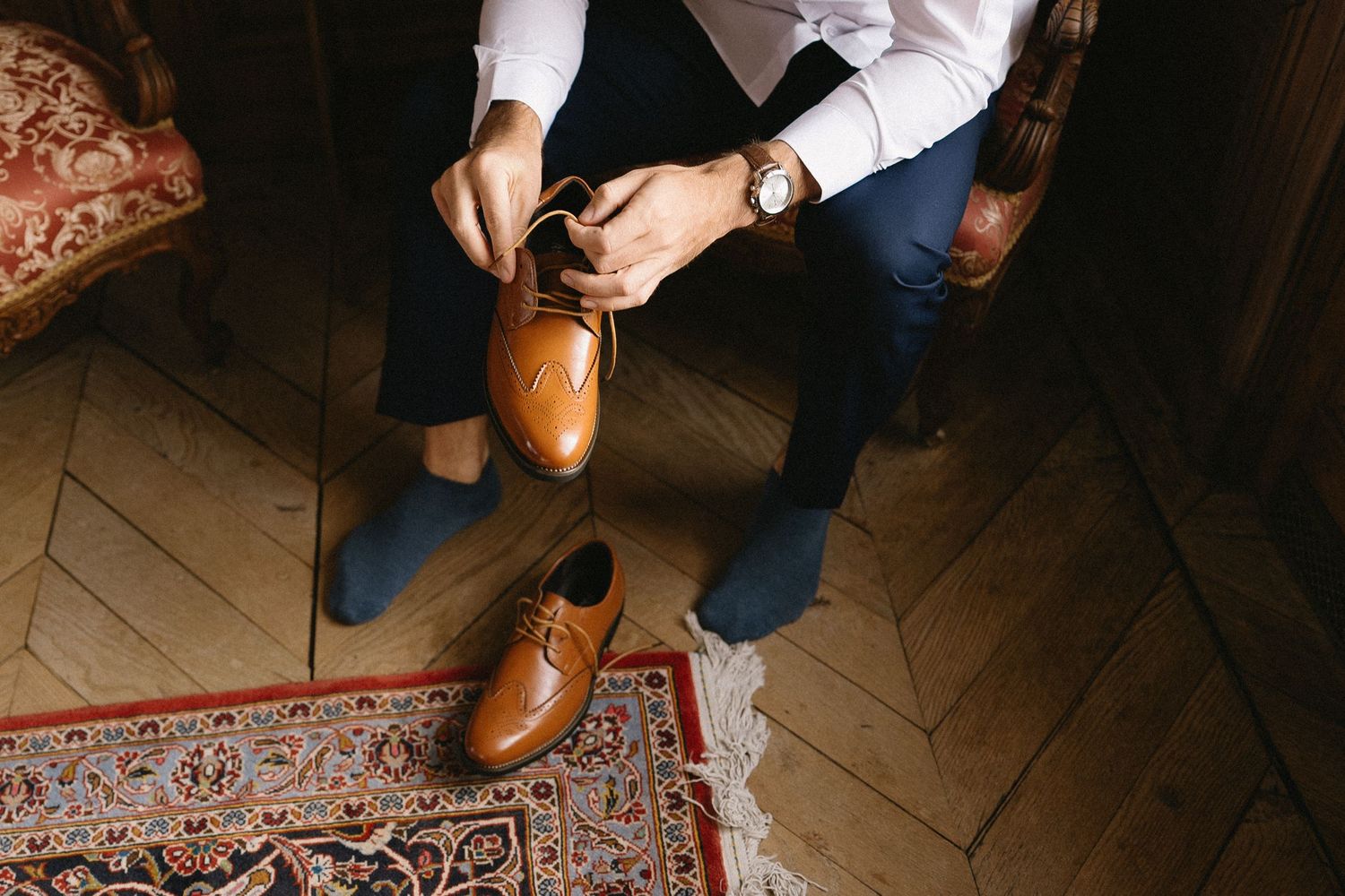 Close-up detail of brown leather boots and clothing on a wooden floor.