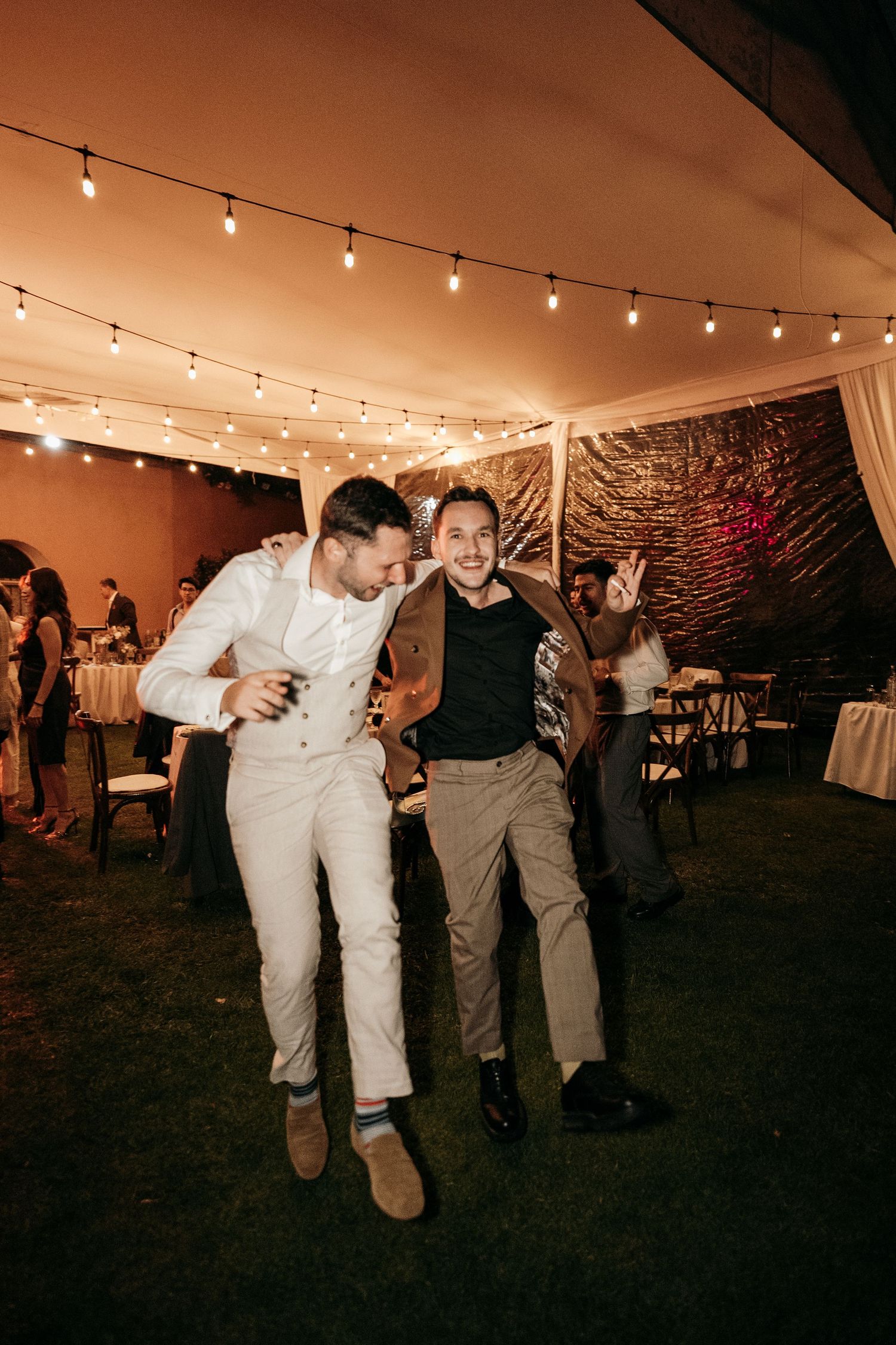 Wedding guests dancing under a tent with string lights at night.