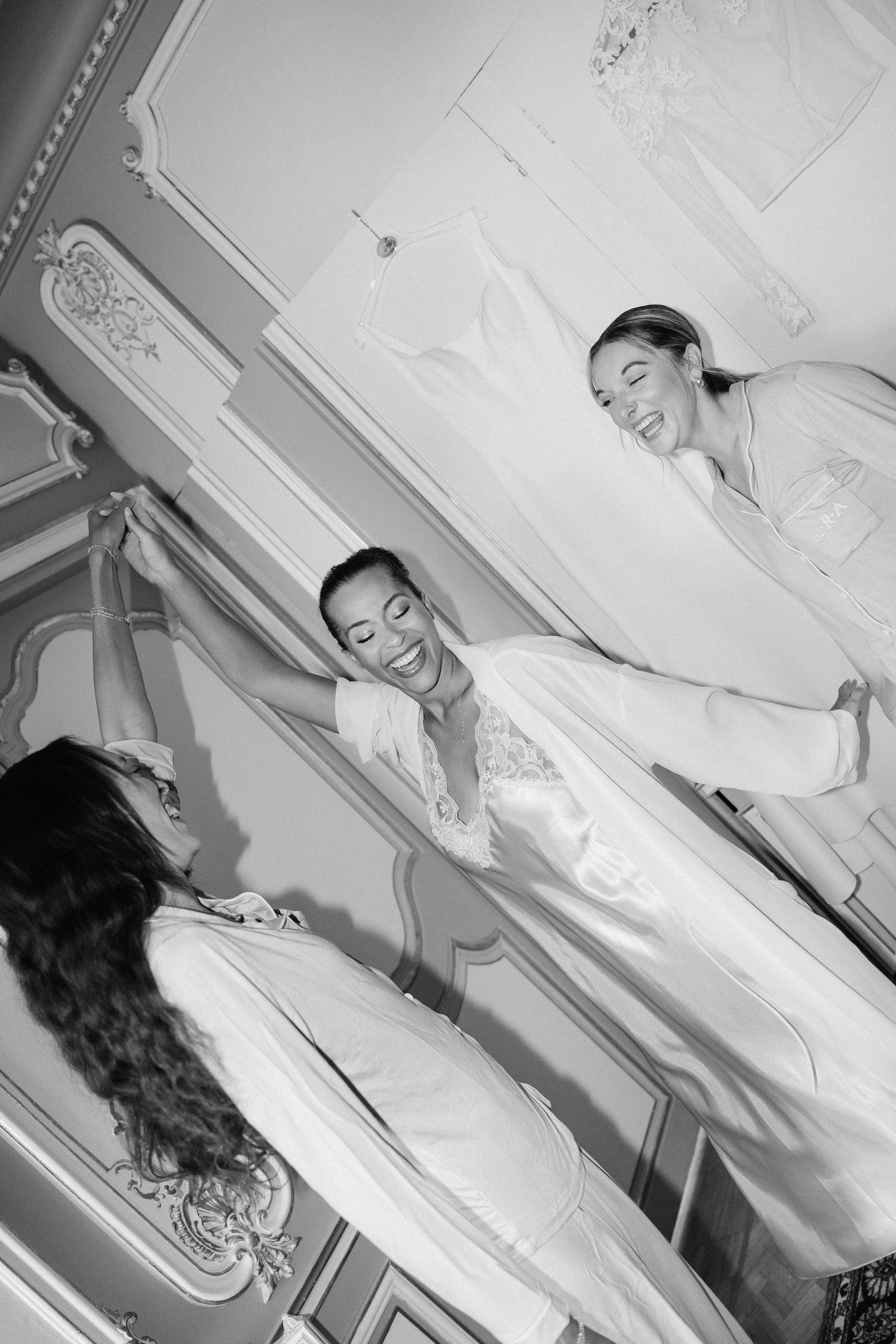 A black and white photo series showing someone trying on a flowing white wedding dress in a bridal fitting room.