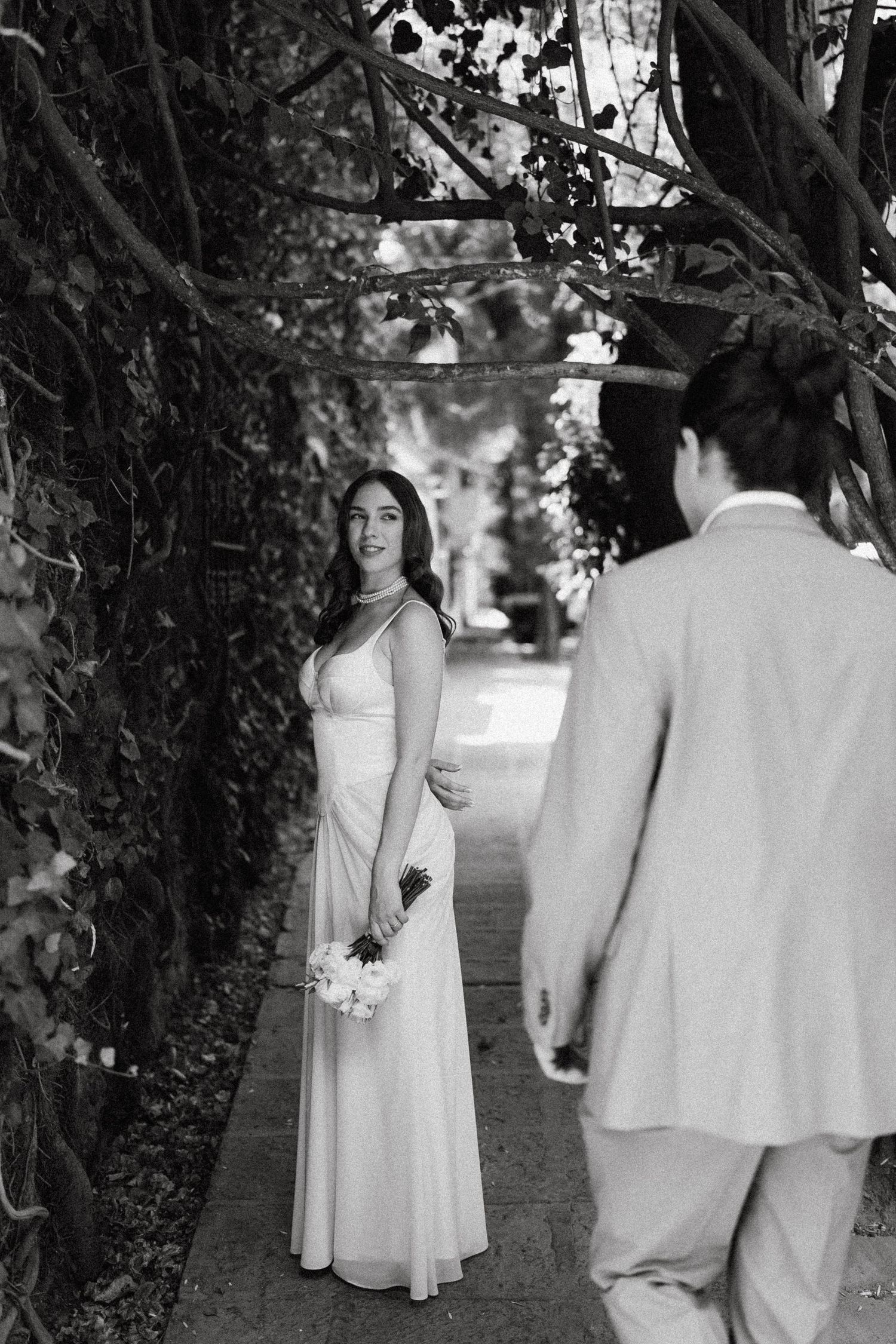 Black and white wedding photos showing a couple meeting in a garden pathway.
