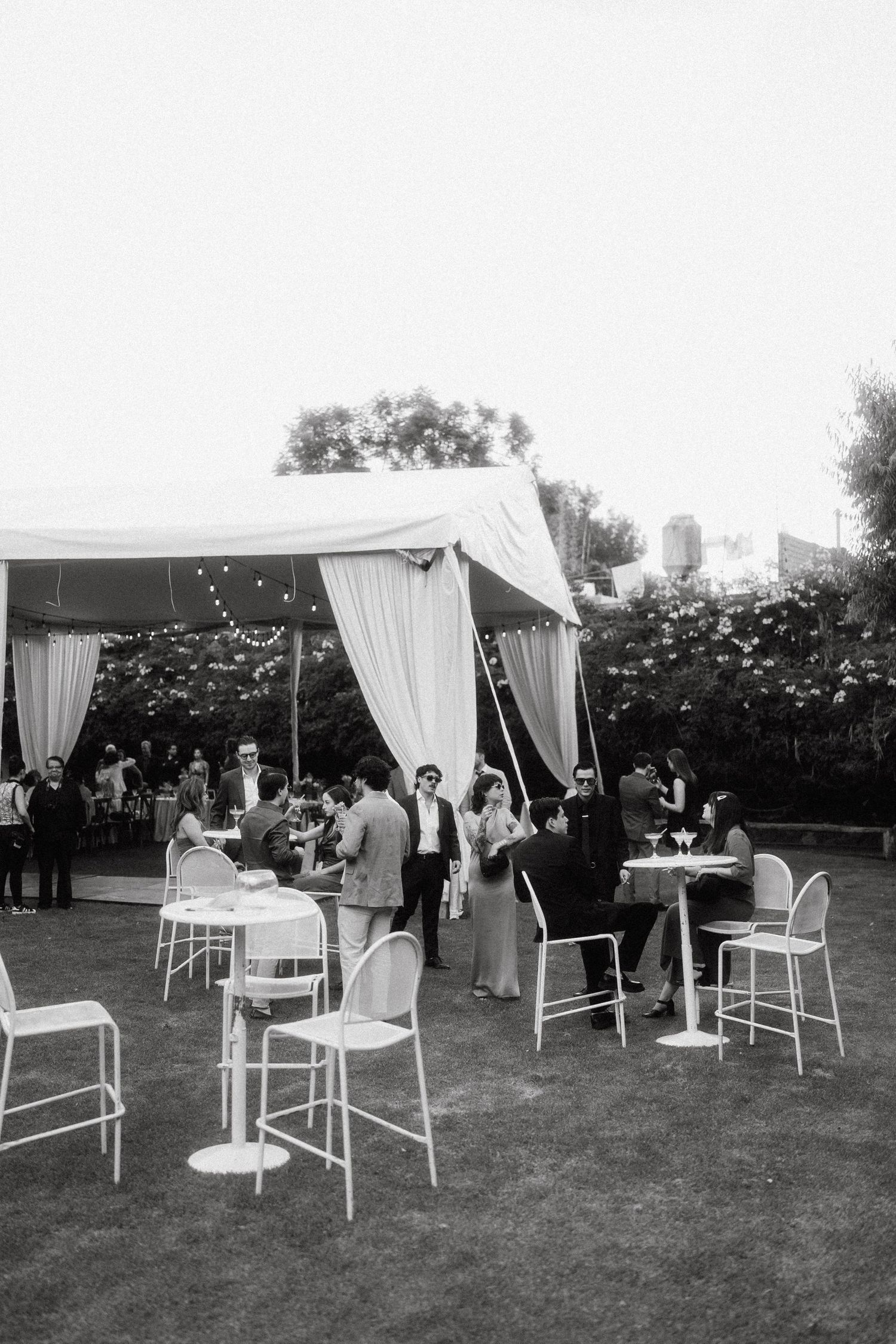 Black and white photo of an outdoor wedding reception with white furniture and draped cabanas.
