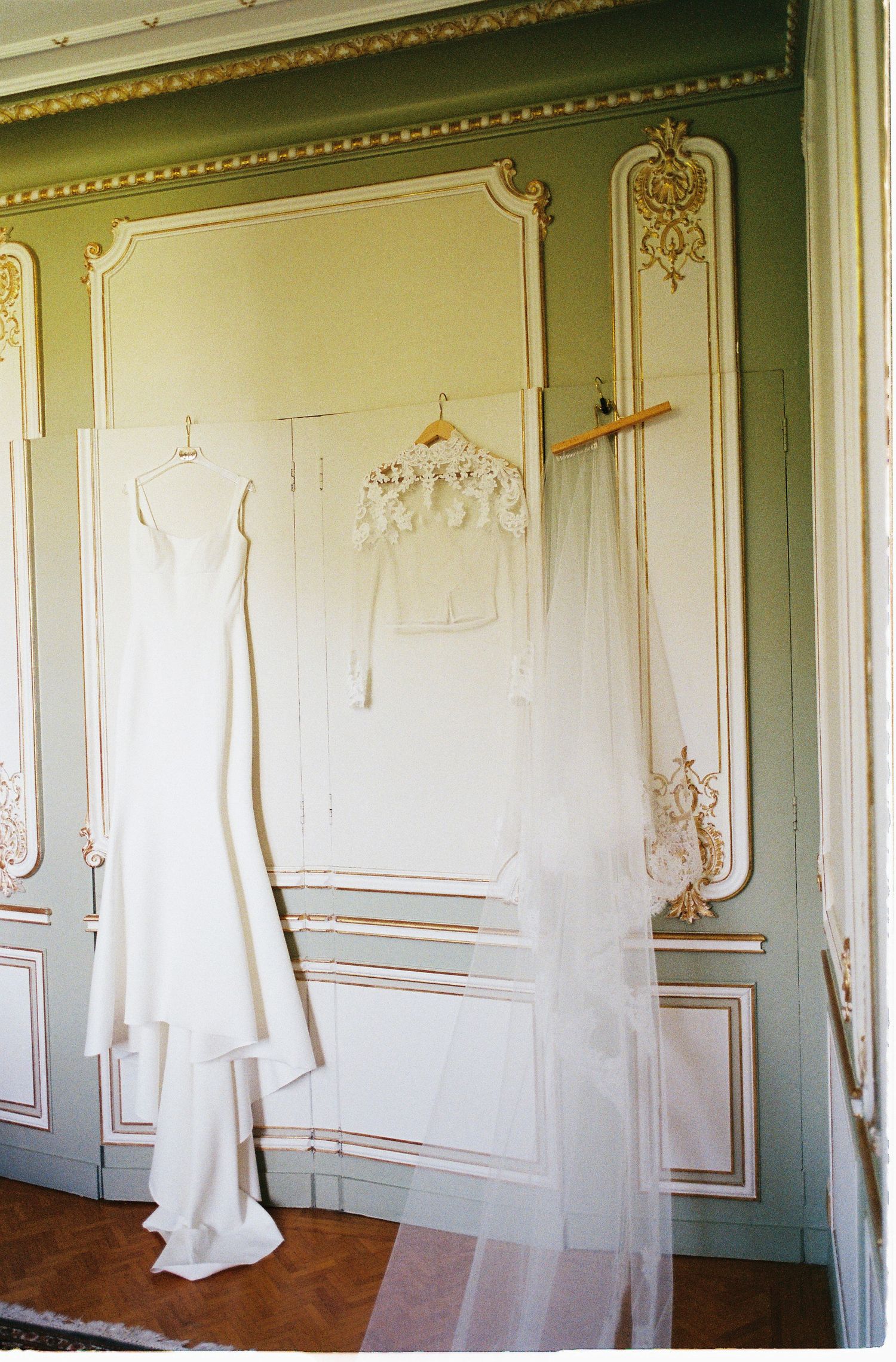 A series of white wedding dresses hanging on display against ornate cream-colored walls with gold trim detailing.