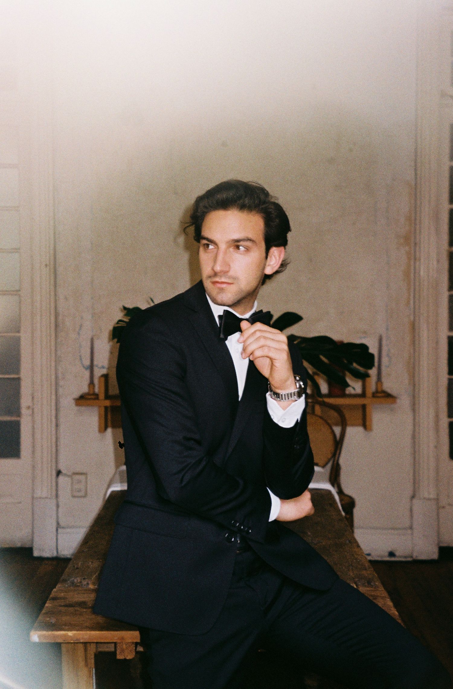 Moody black and white portrait series showing figure in dark suit against light wall.