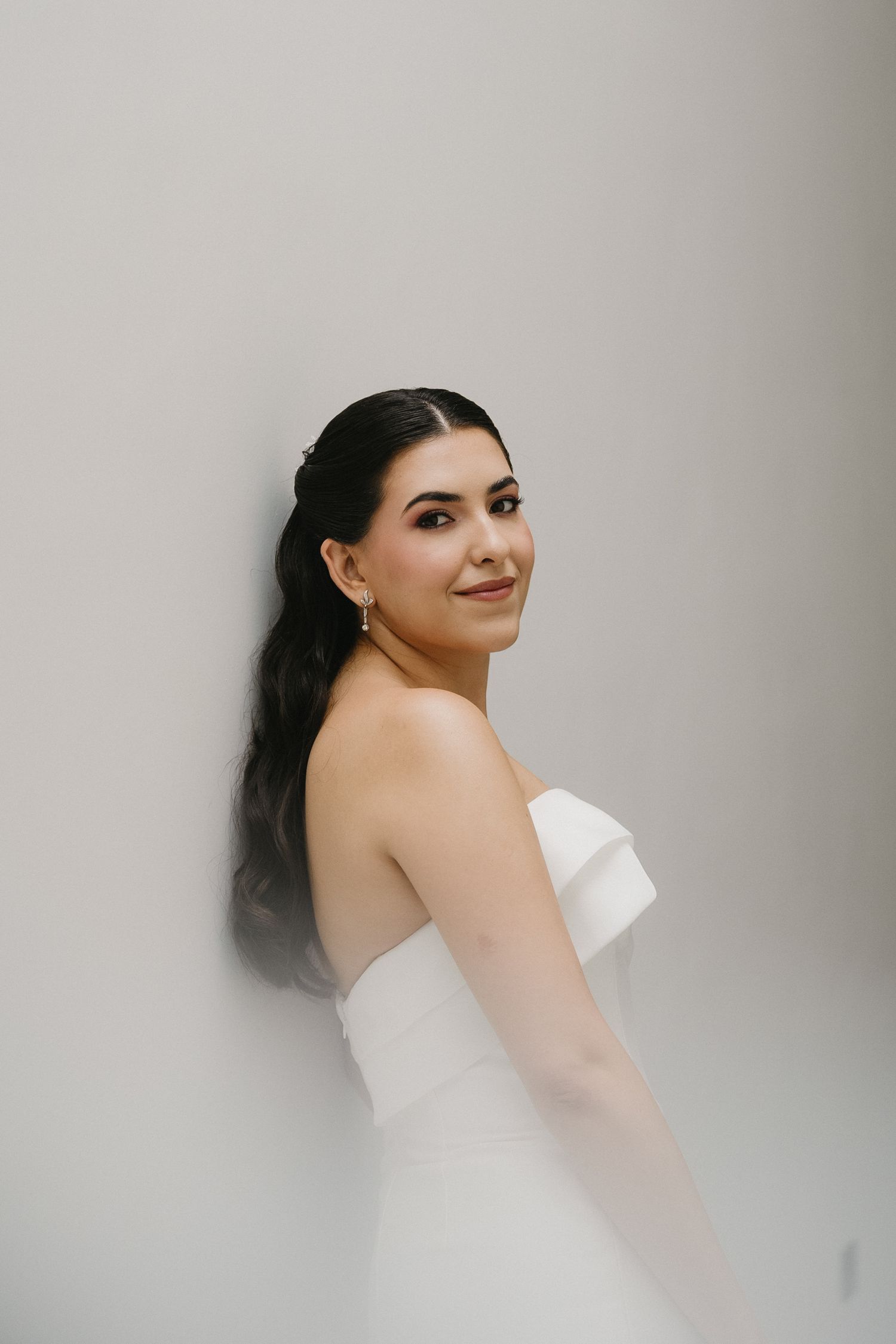 A bride in a white dress poses against a light gray background in an artistic portrait series.