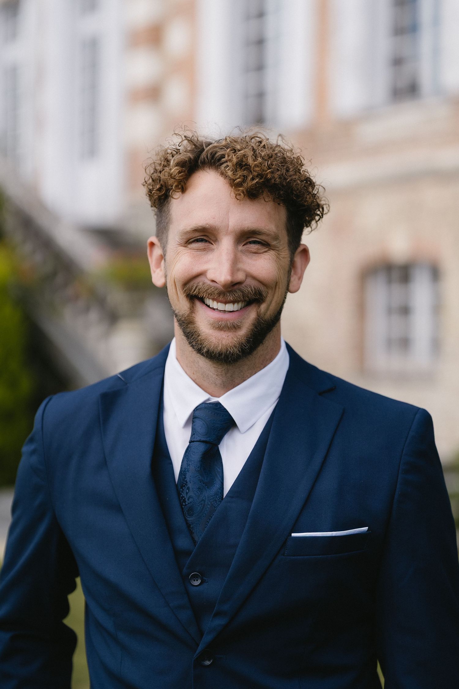 A person in a navy suit and tie smiles warmly at the camera.
