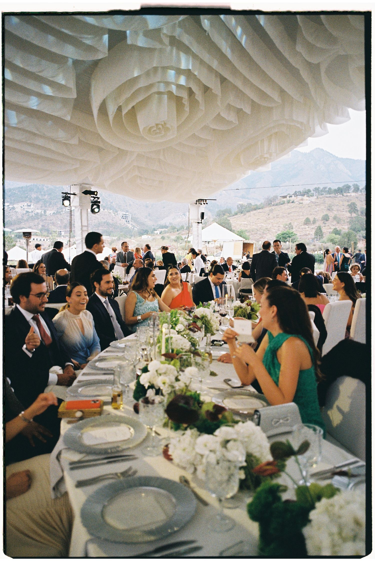 Long banquet tables set with white linens and floral centerpieces under an elegant draped tent ceiling.